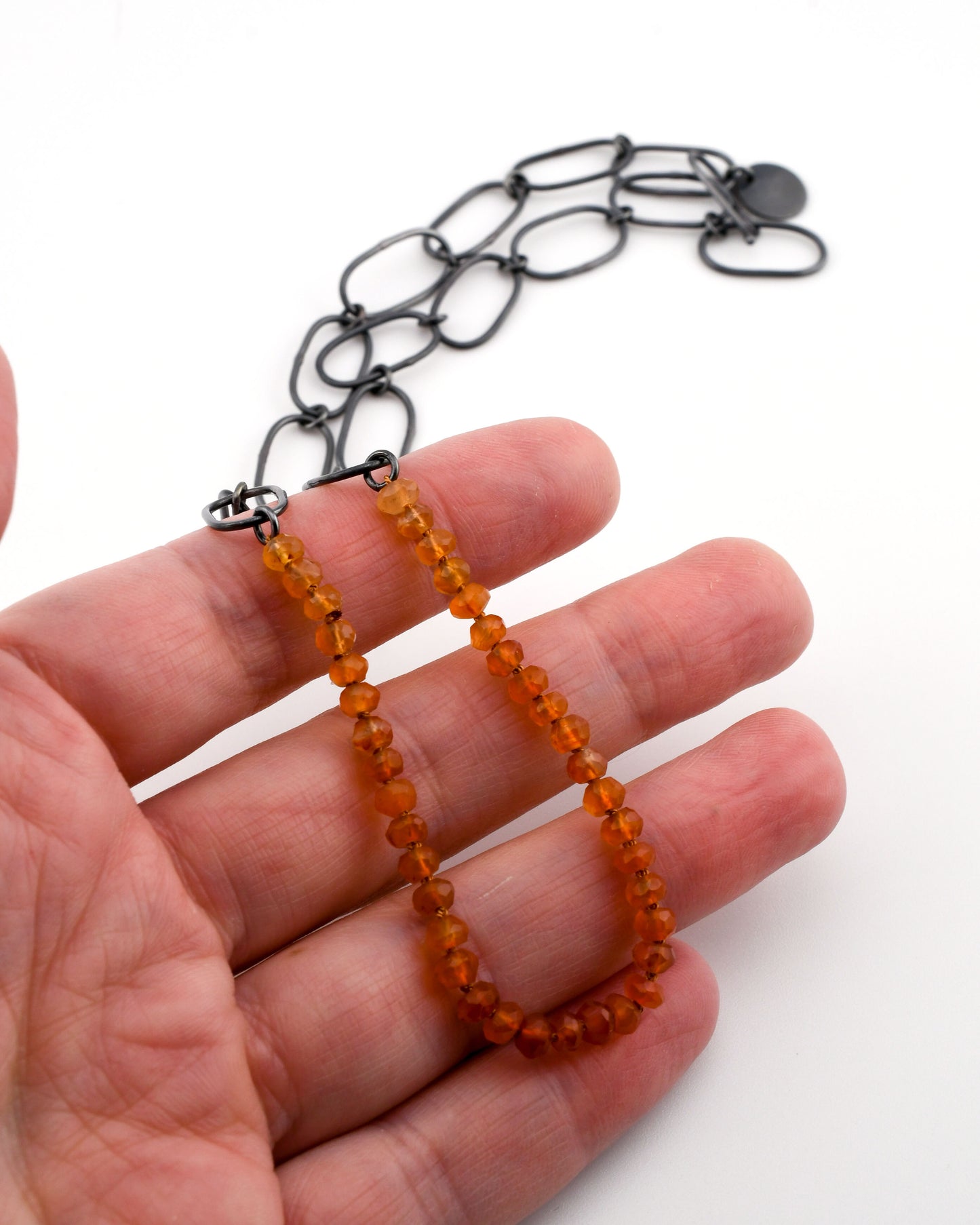 Orange beaded necklace on a hand with a white background