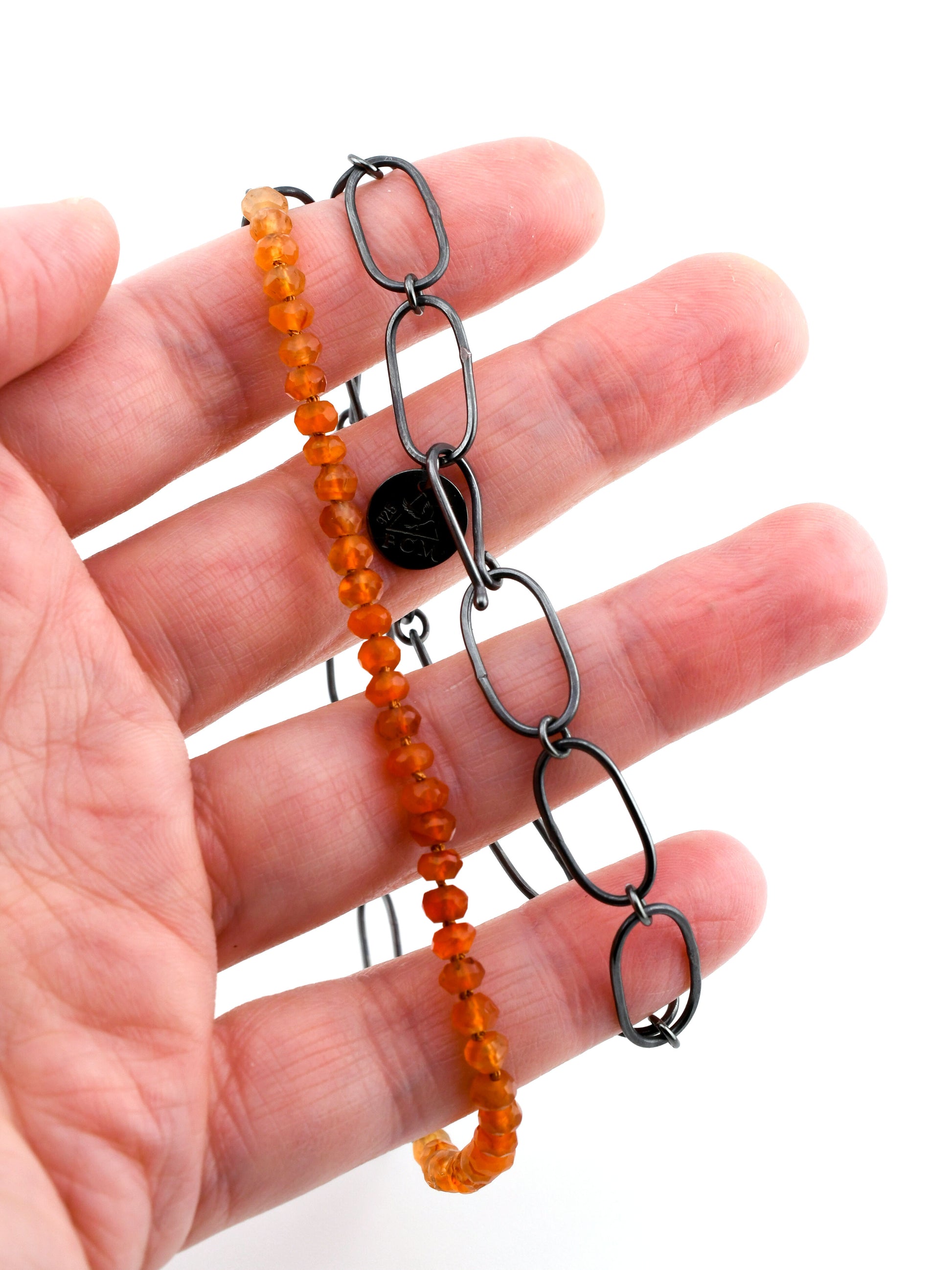 Hand holding an orange beaded necklace with black chain links, on a white background.