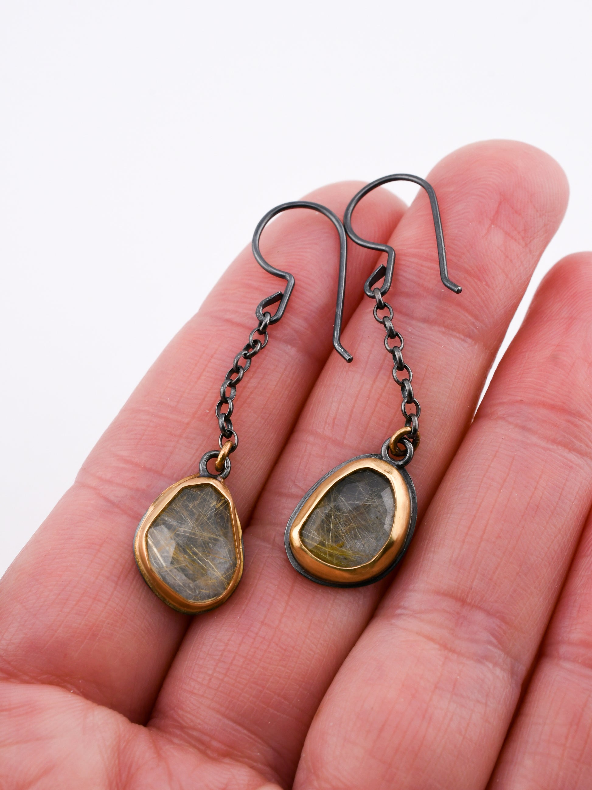 Pair of earrings with gemstones held in a hand against a white background