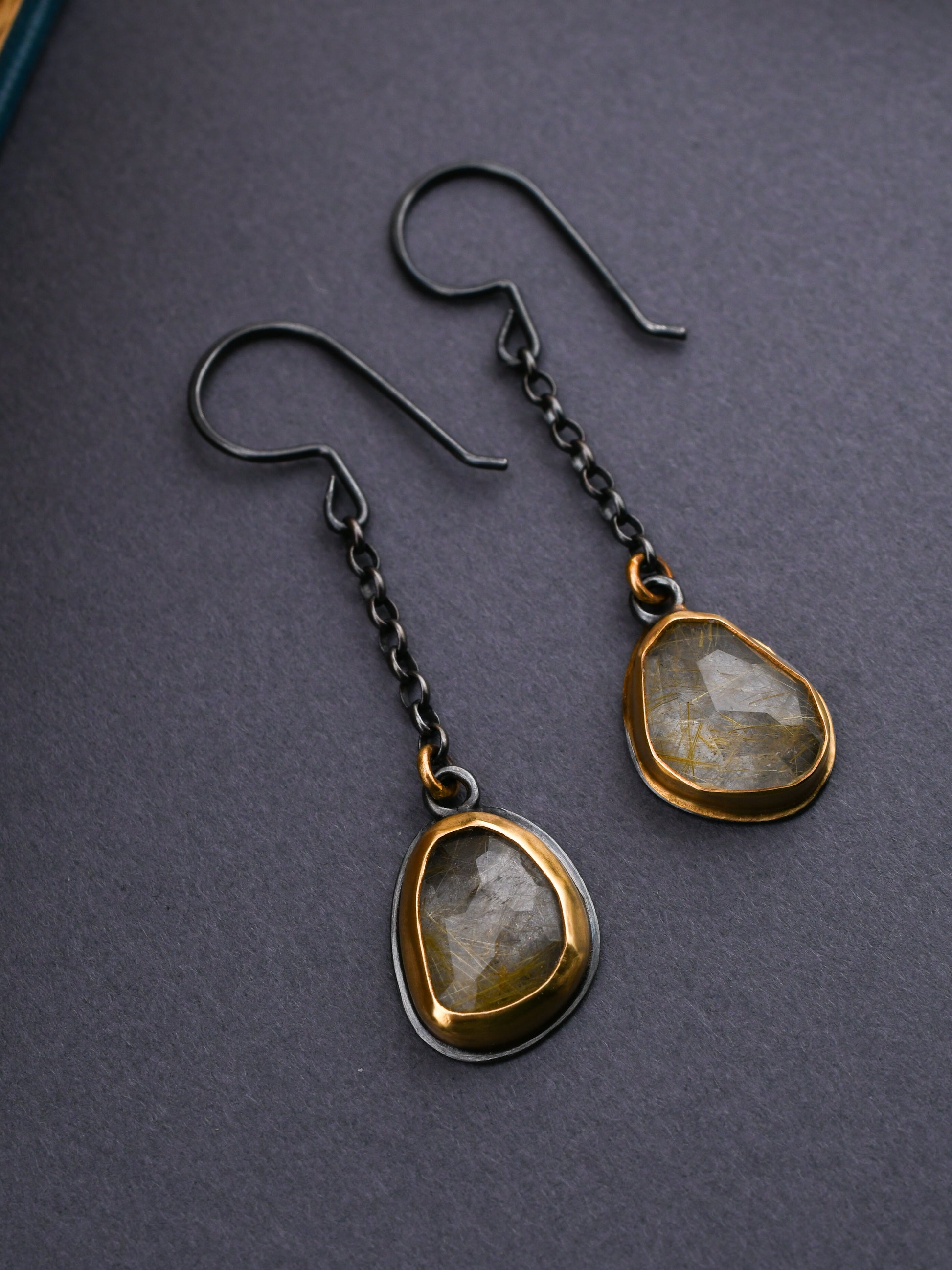 Black and gold earrings with chain details and rutilated quartz on a dark gray background