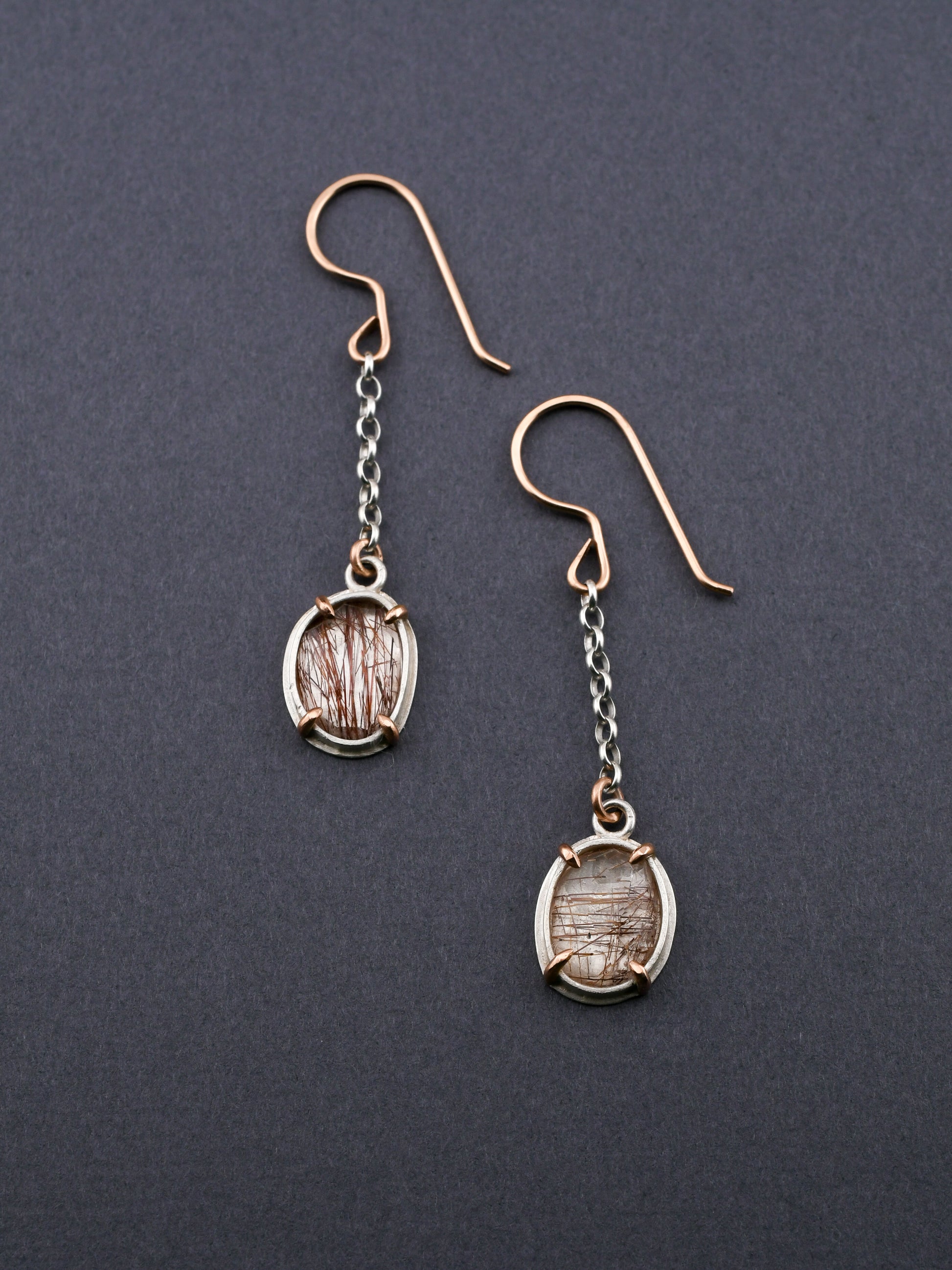 Red rutilated quartz earrings in silver and gold with chain details on a dark gray background