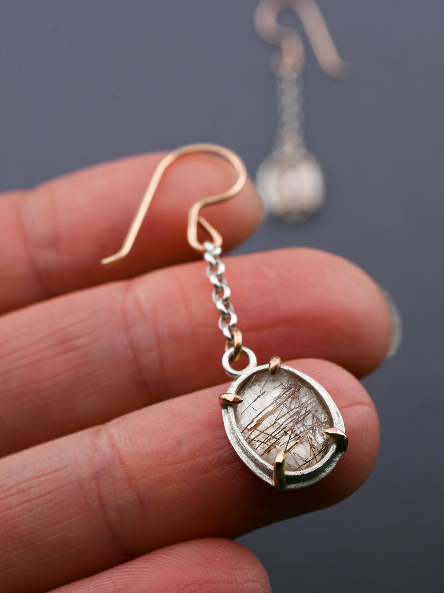 Close-up of a hand holding a unique earring with a dark background