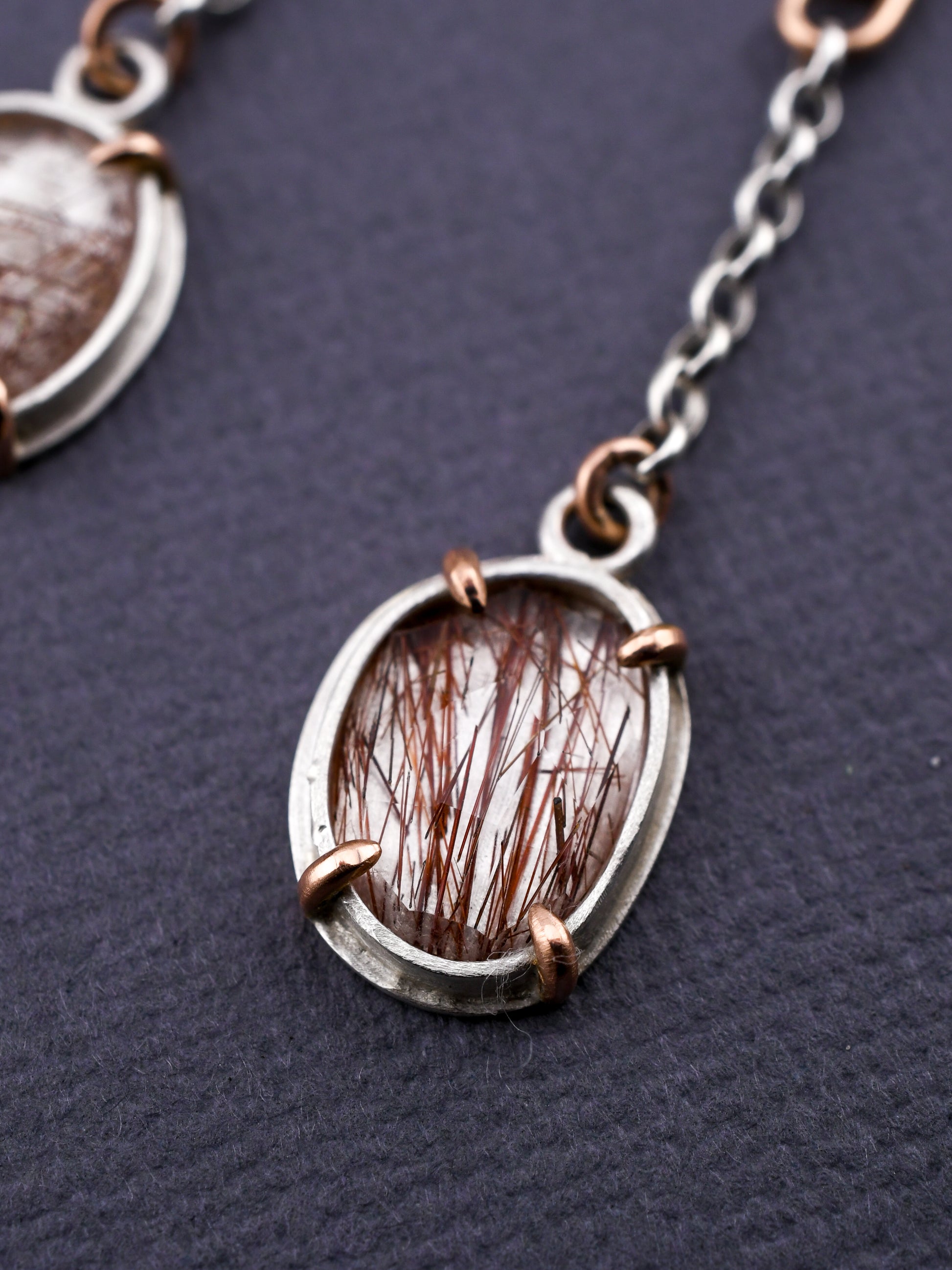 Closeup of rutilated quartz earring in silver  and rose gold on a dark gray background