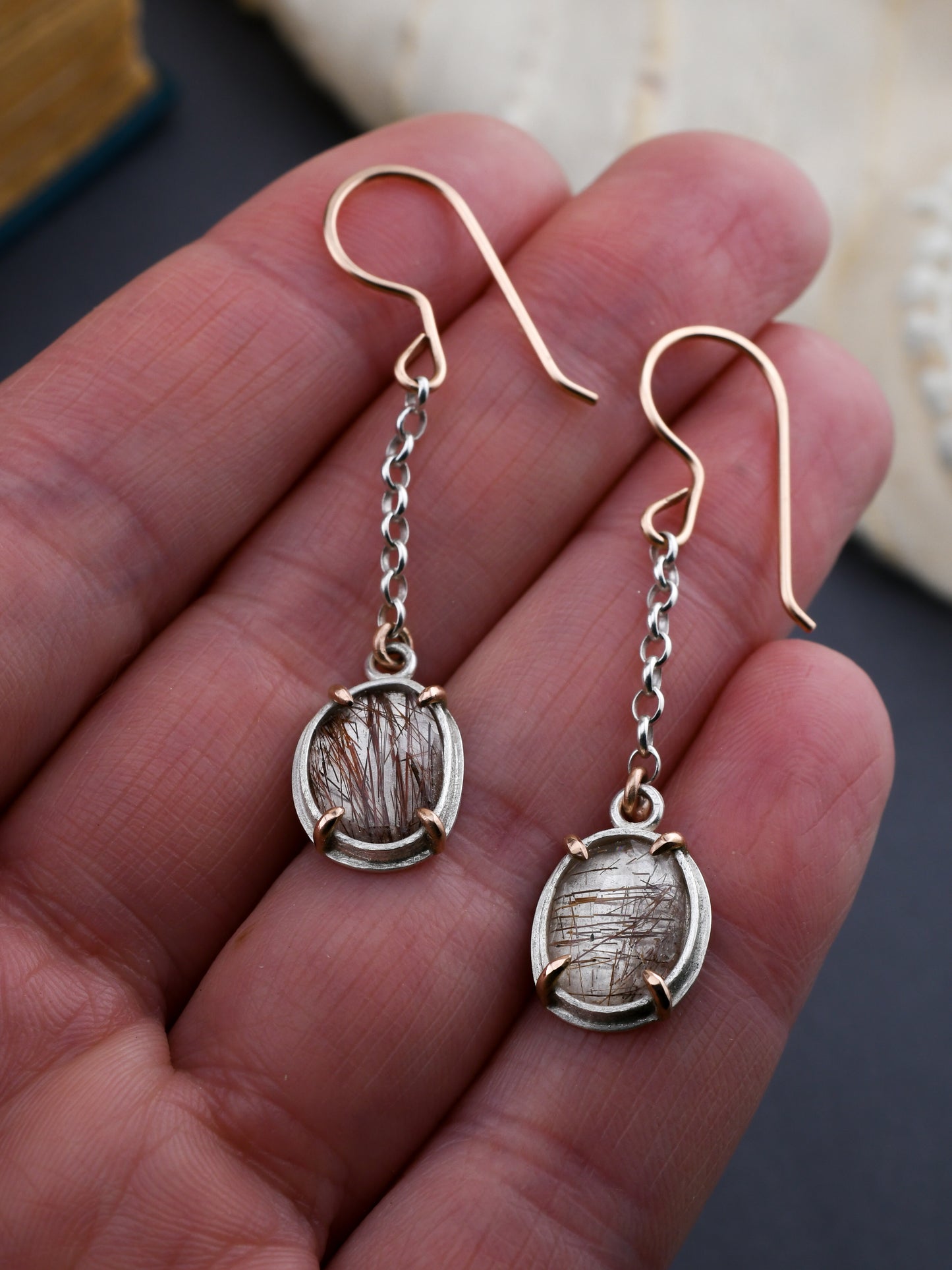 Silver earrings with chain drops held in a hand against a neutral background