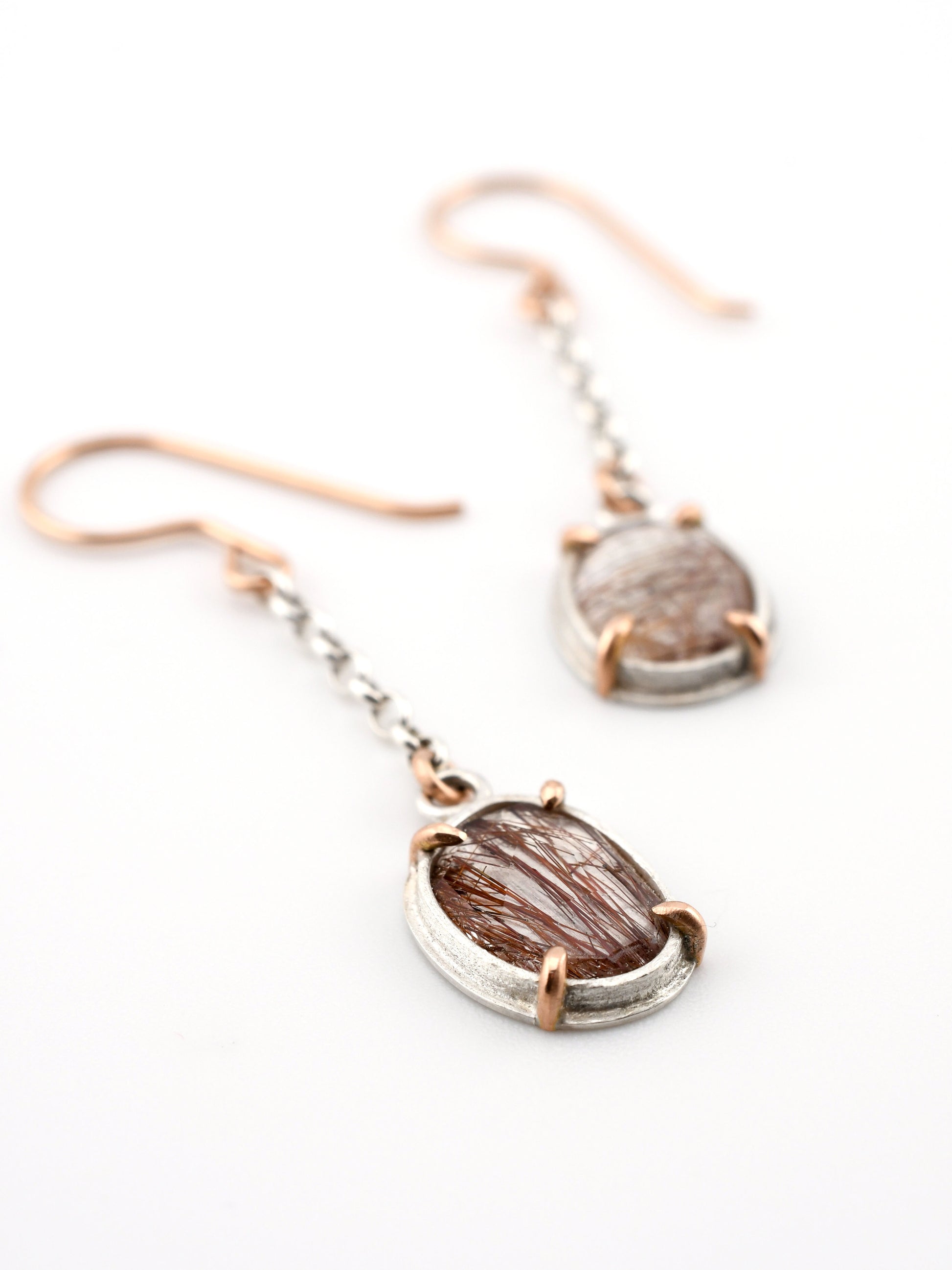 Pair of earrings with red rutilated quartz gemstones on a white background