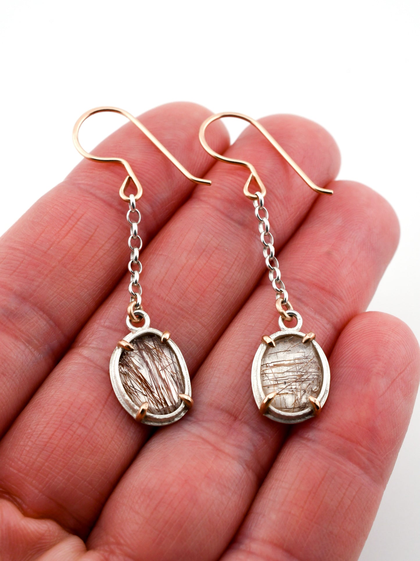 Gold and silver earrings held in a hand against a white background