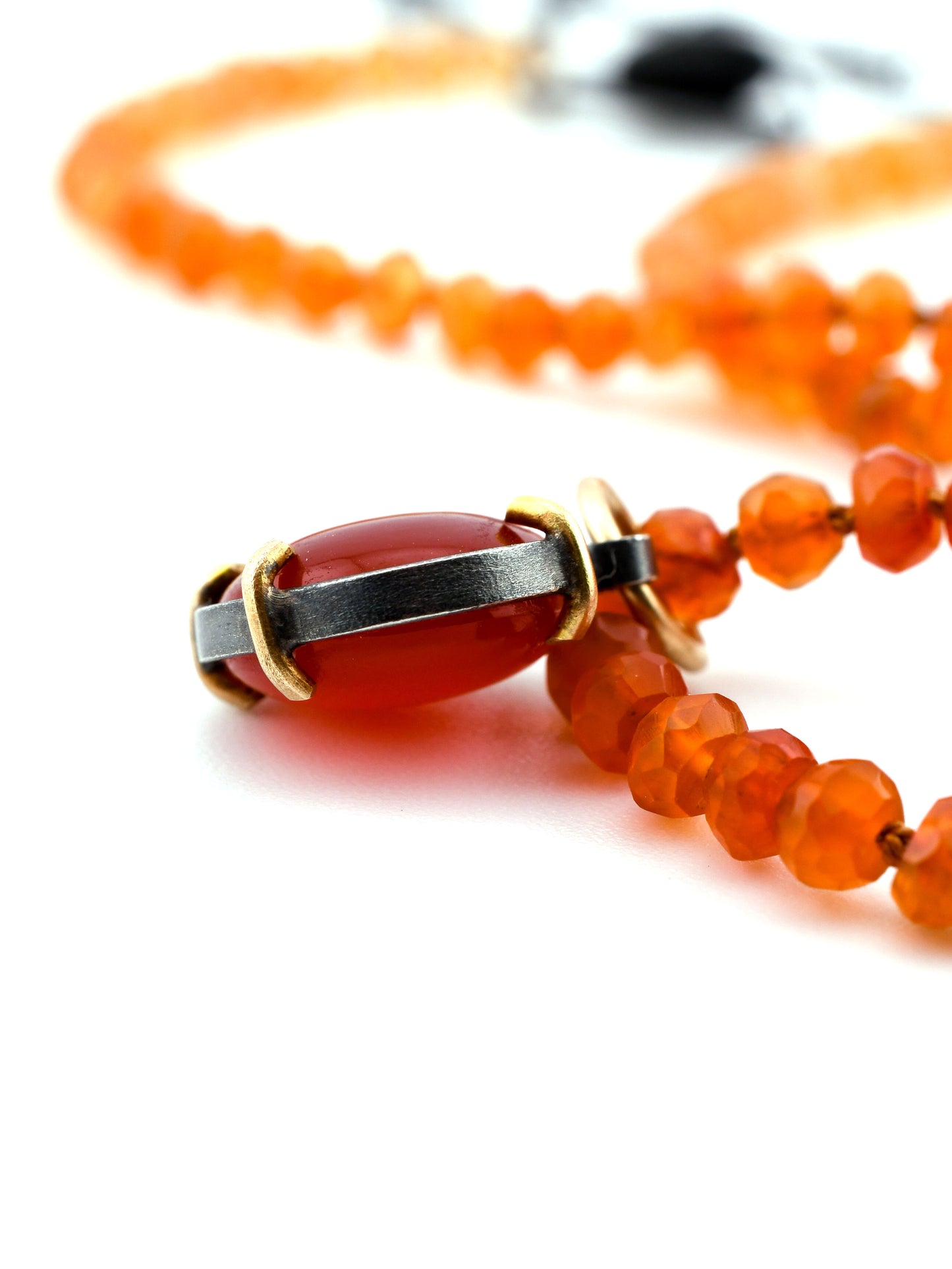 Close-up of a necklace with orange beads and a silver and gold pendant on a white background