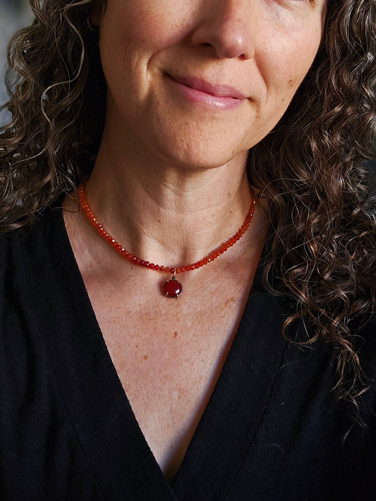 Close-up of a woman wearing a red beaded necklace with a large red gemstone pendant.