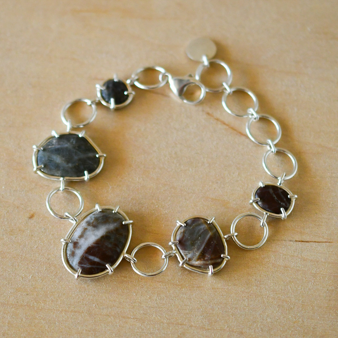 Silver bracelet with textured beach stones on a pale wood surface