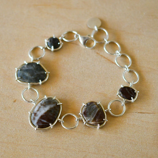 Silver bracelet with textured beach stones on a pale wood surface