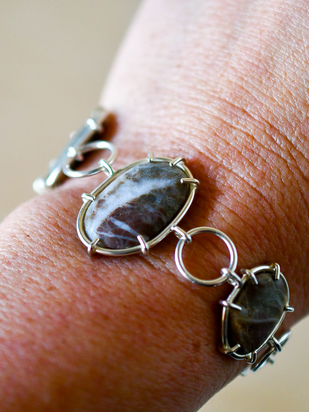 Silver bracelet with beach stones on a wrist against a neutral background