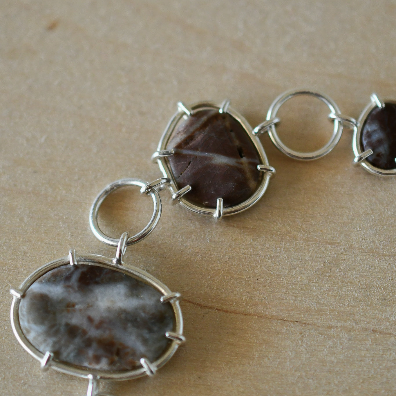 Silver bracelet with red and green textured beach stones on a pale wood background