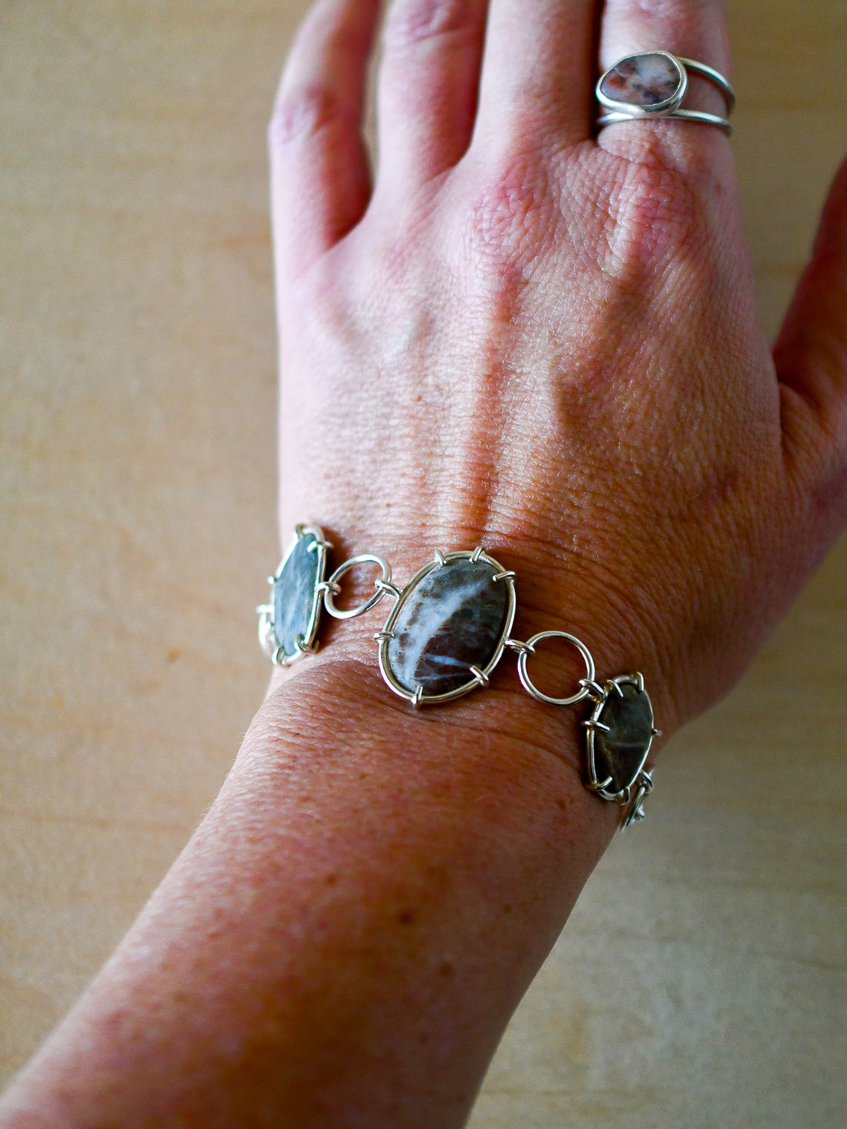 Hand wearing a silver bracelet with beach stones on a beige background