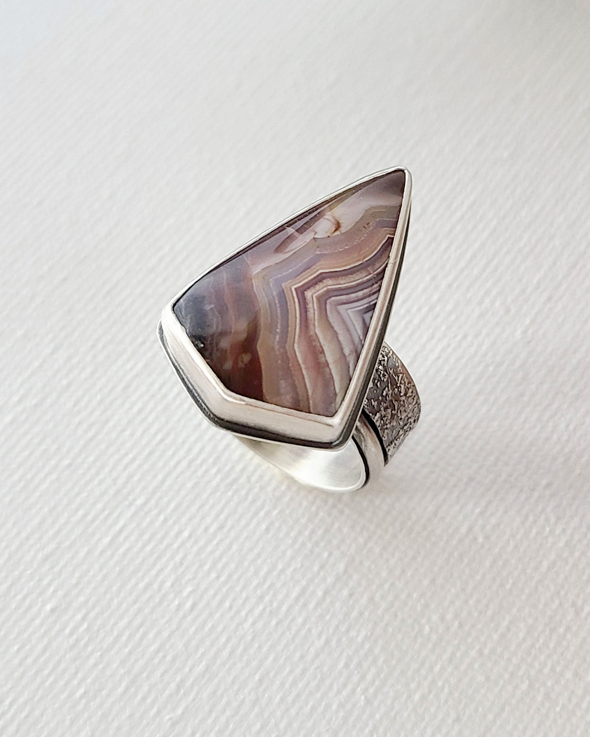Triangular purple laguna lace agate ring shown from above on a textured white surface