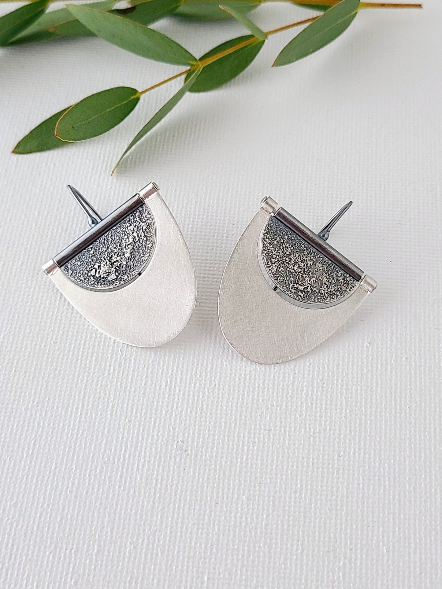 large silver earrings with textured and oxidized half-circles within half-ovals with a bright brushed surface