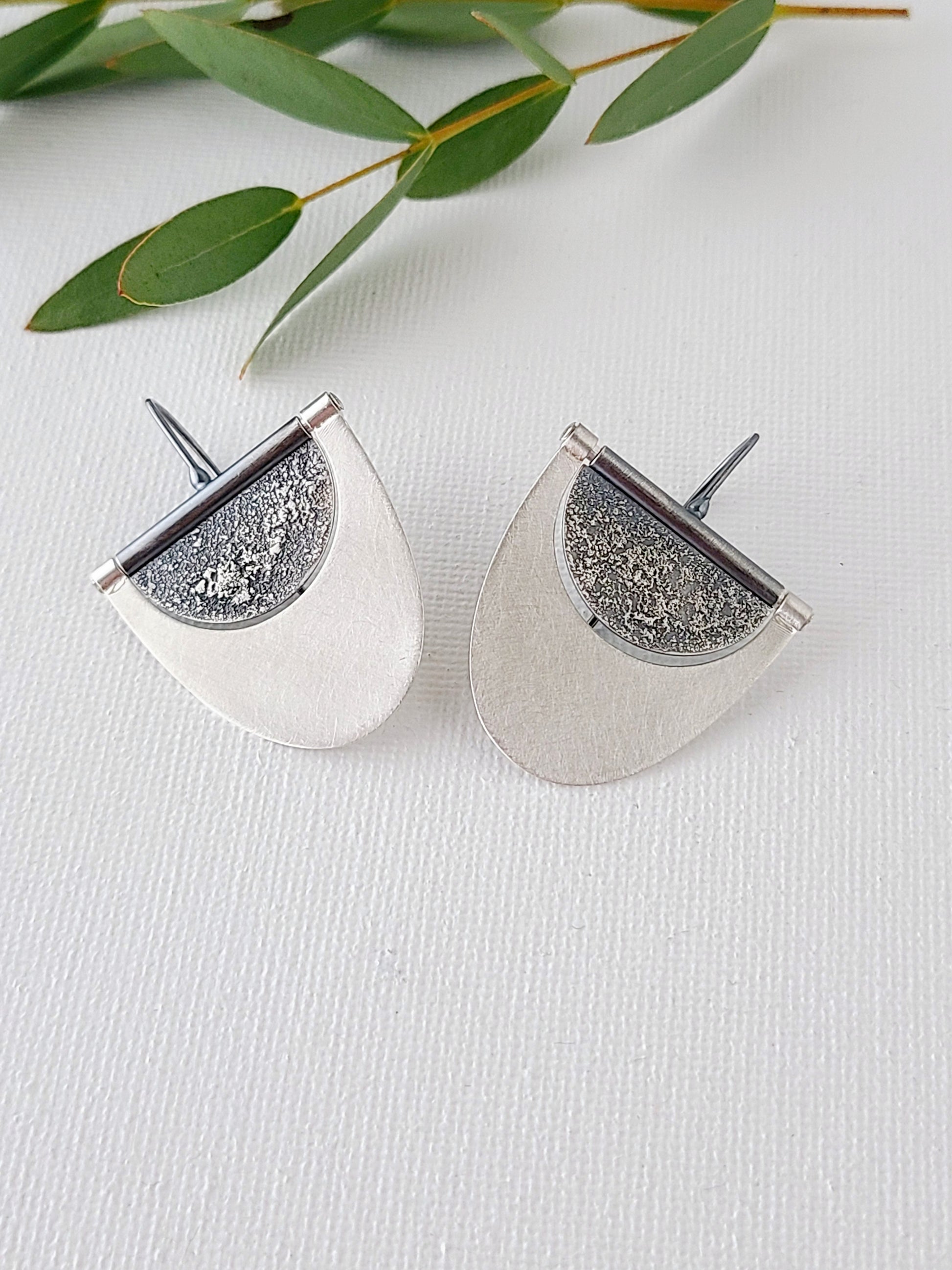large silver earrings with textured and oxidized half-circles within half-ovals with a bright brushed surface