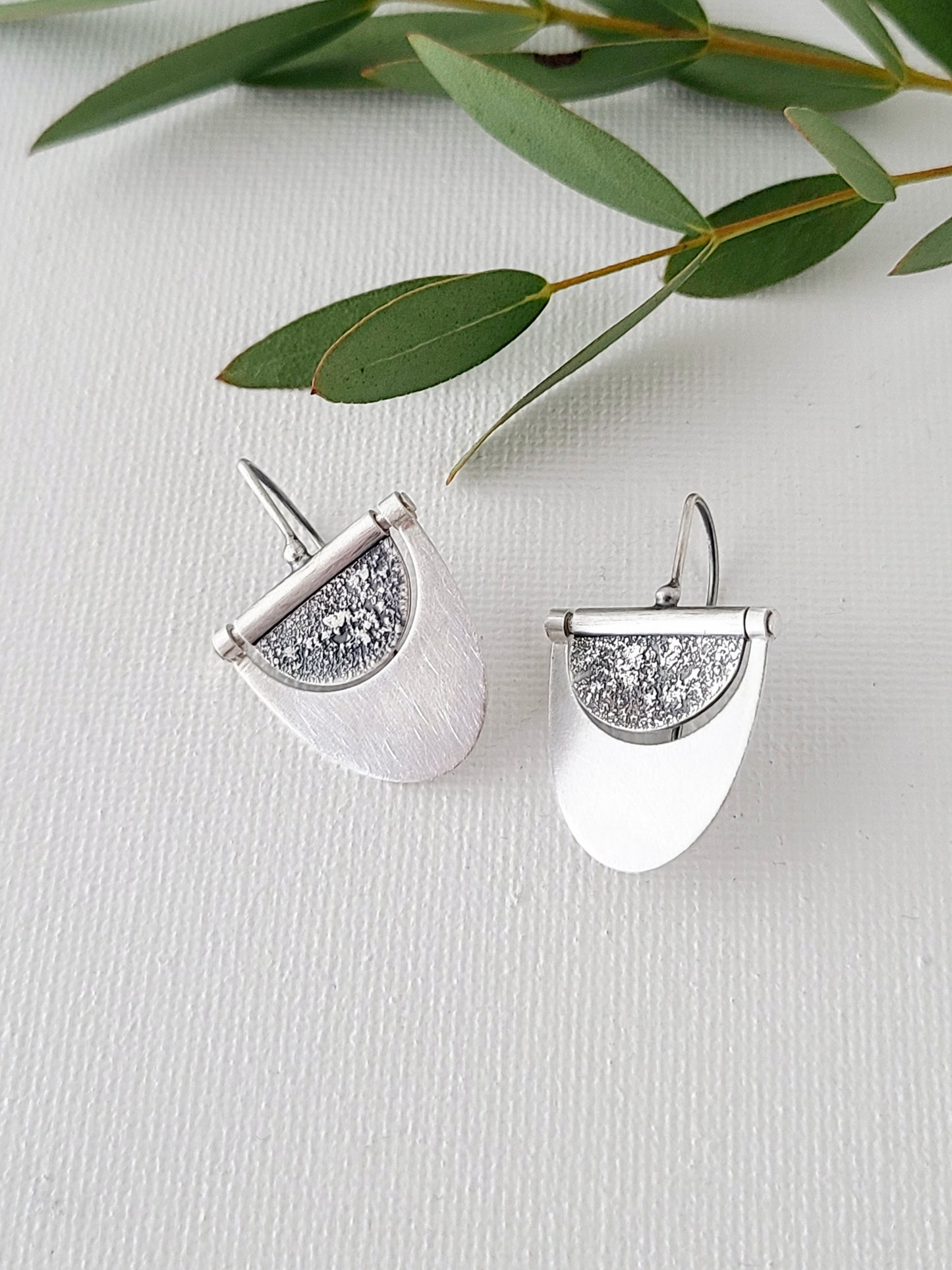 Medium silver earrings with textured and oxidized half-circles within half-ovals with a bright brushed surface