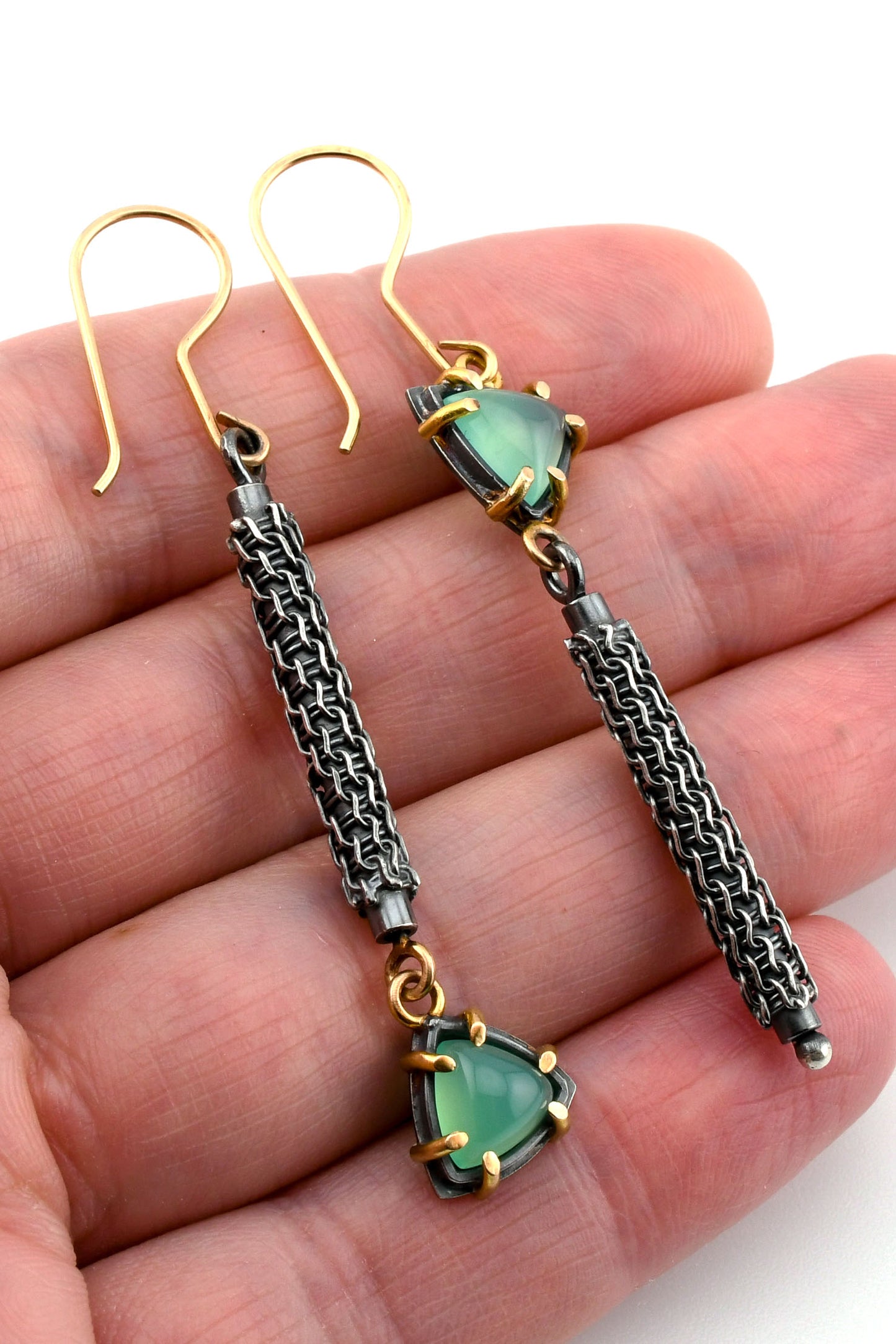 Pair of earrings with green gemstones and woven details held in a hand.