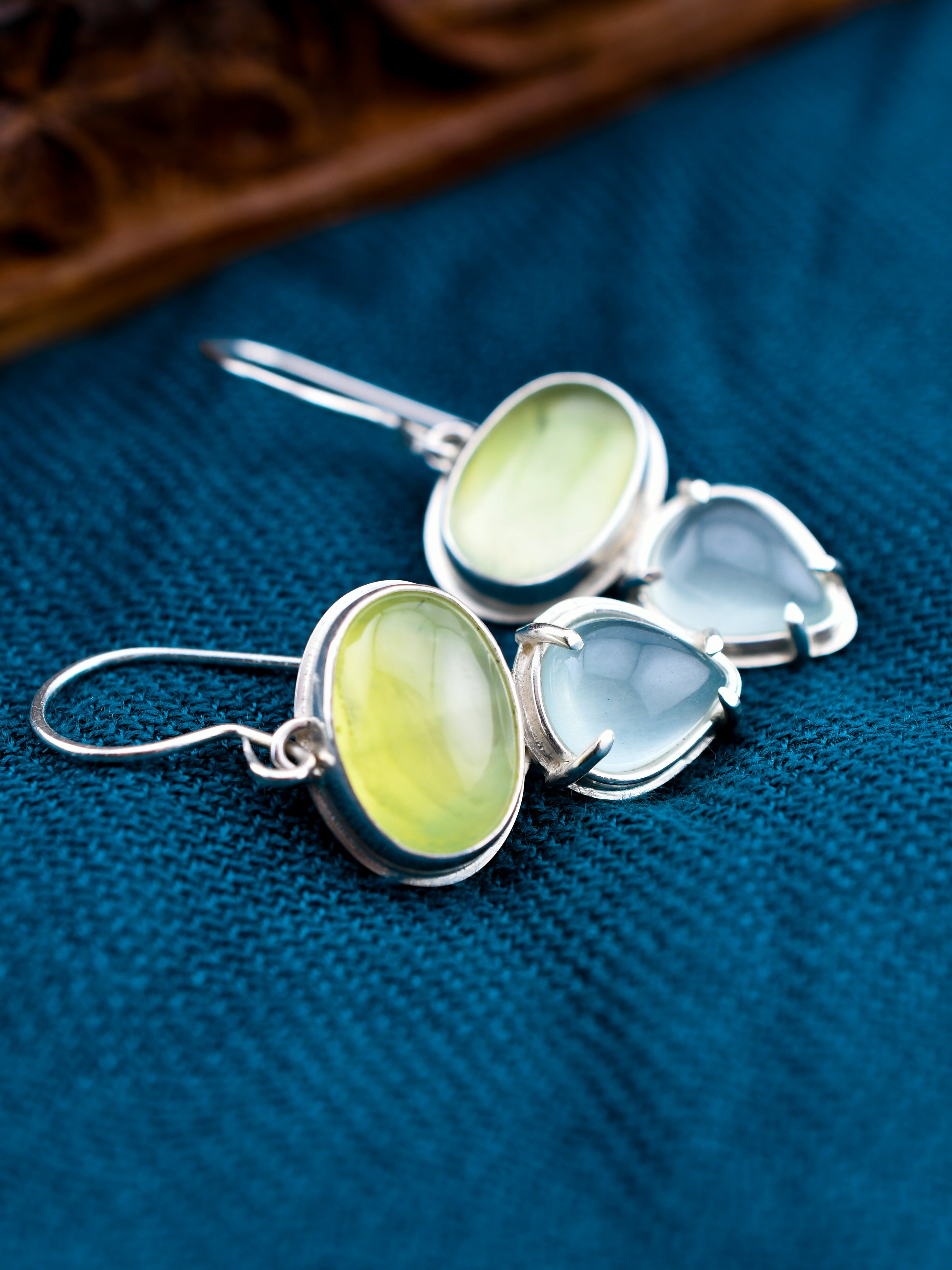 Silver earrings with green and blue stones on a blue fabric background