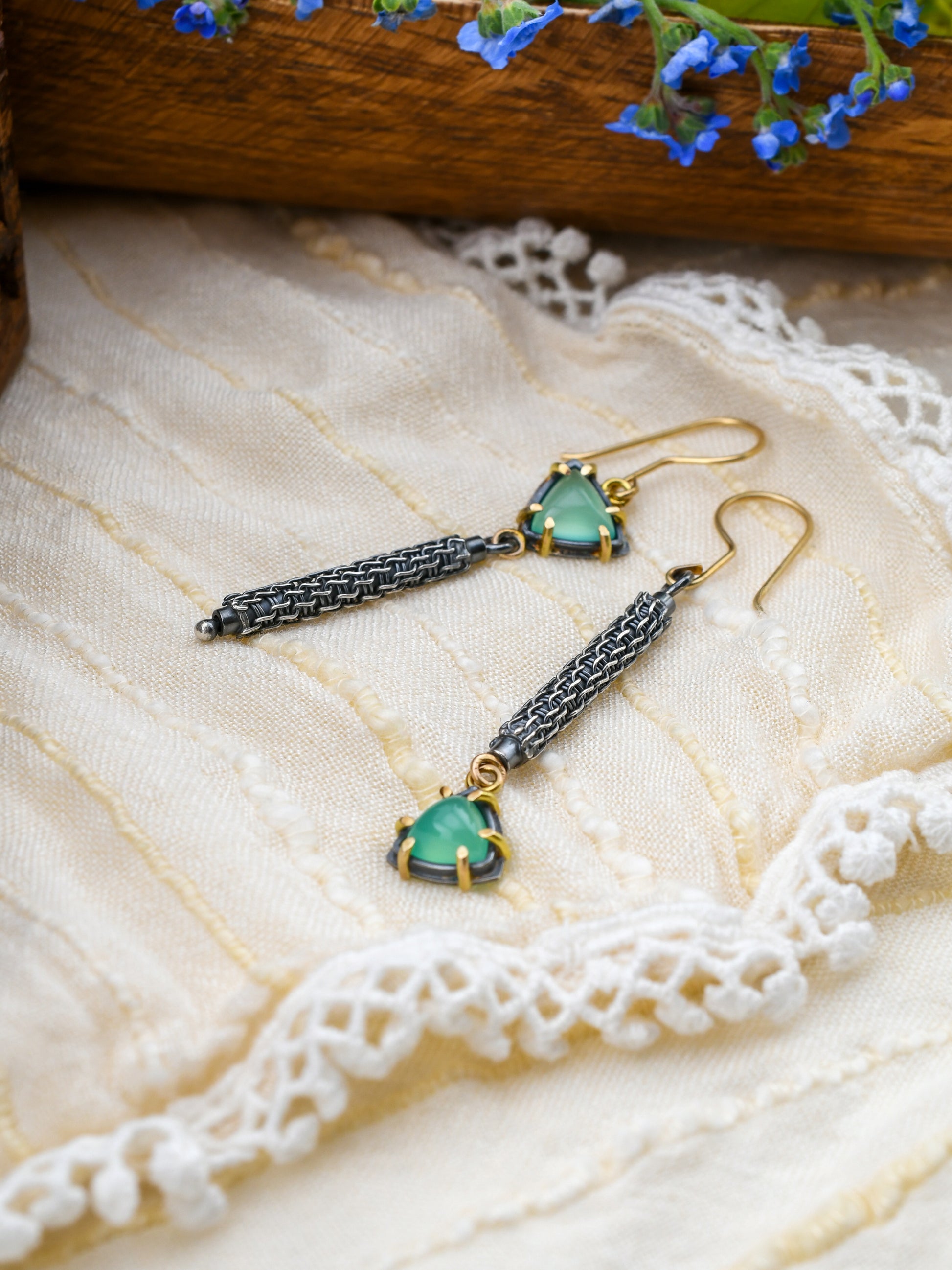 Pair of earrings with green gemstones on a lace fabric background