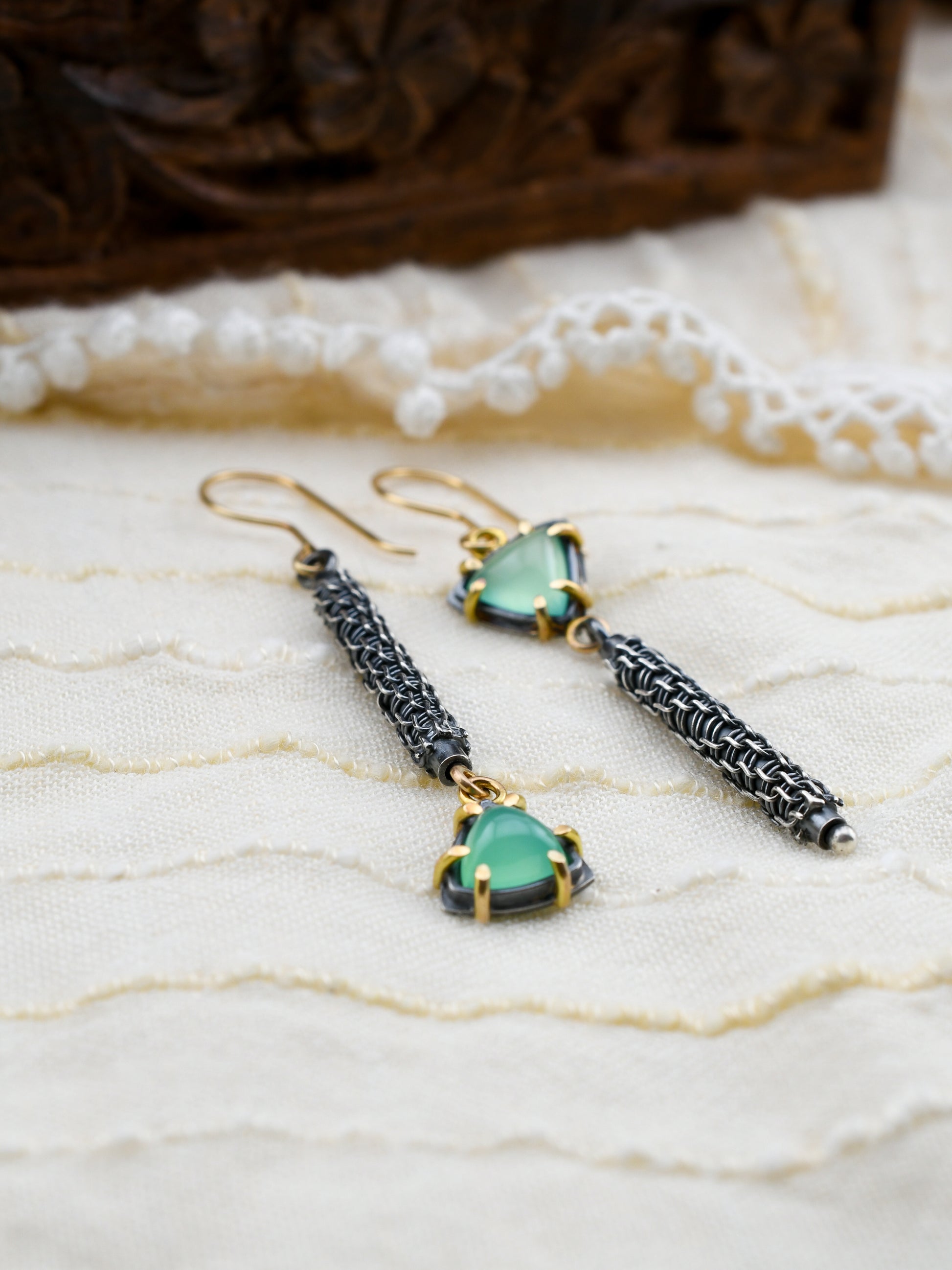 Pair of earrings with green gemstones and woven details on a textured surface.