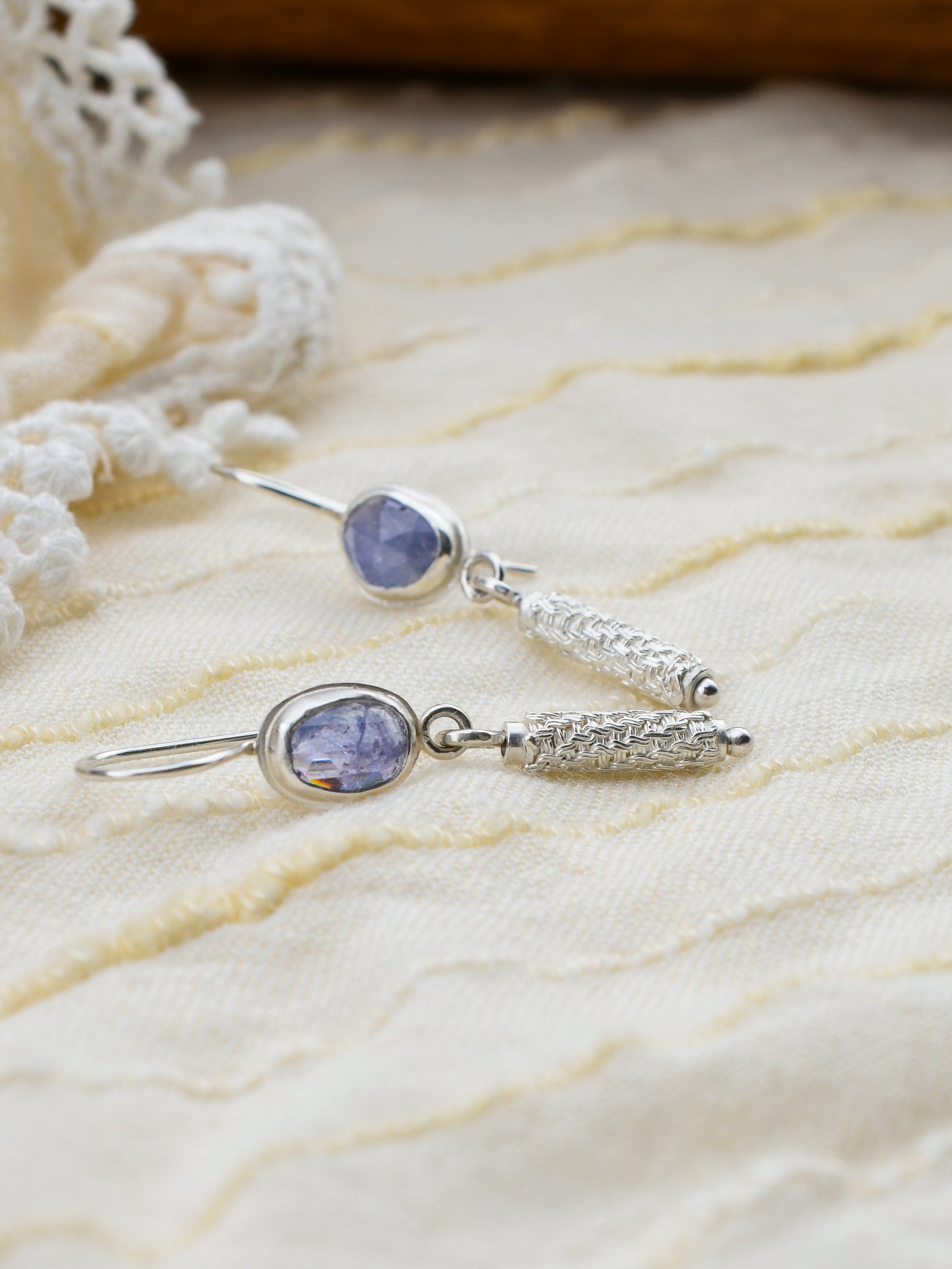 Silver earrings with purple gemstones on a textured beige surface