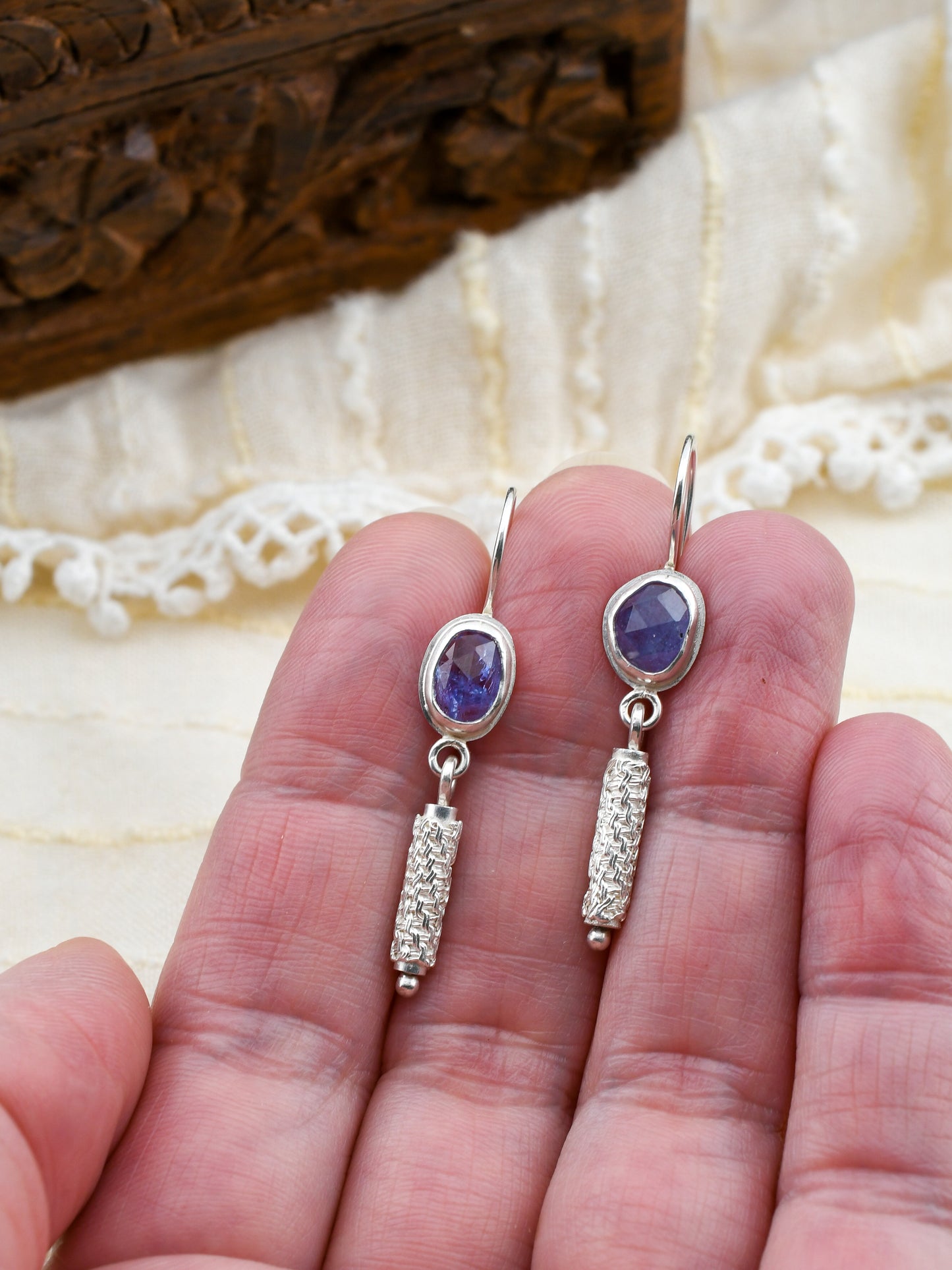 Silver earrings with gemstones held between fingers on a textured surface