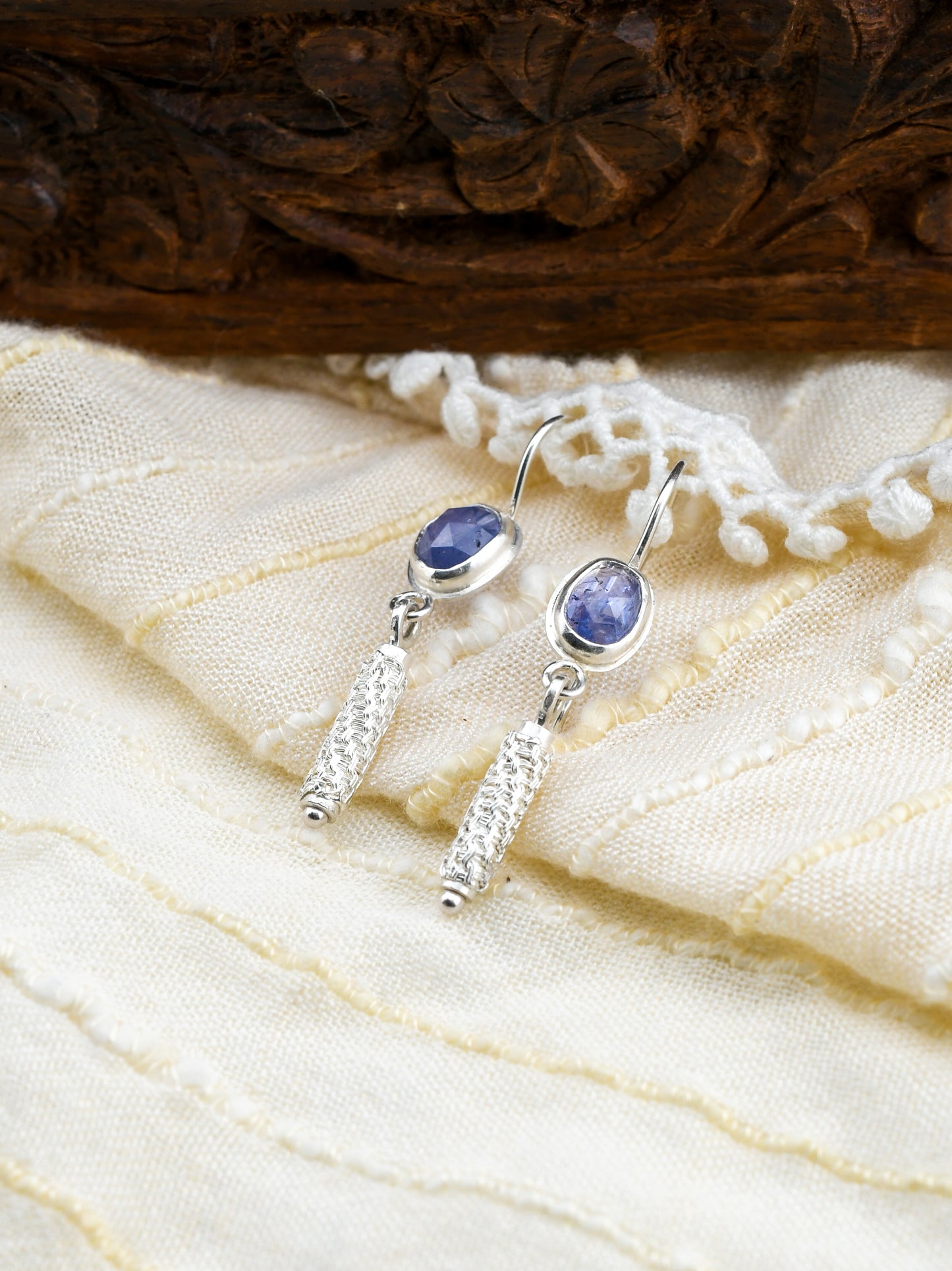 Silver earrings with blue gemstones on a textured fabric background
