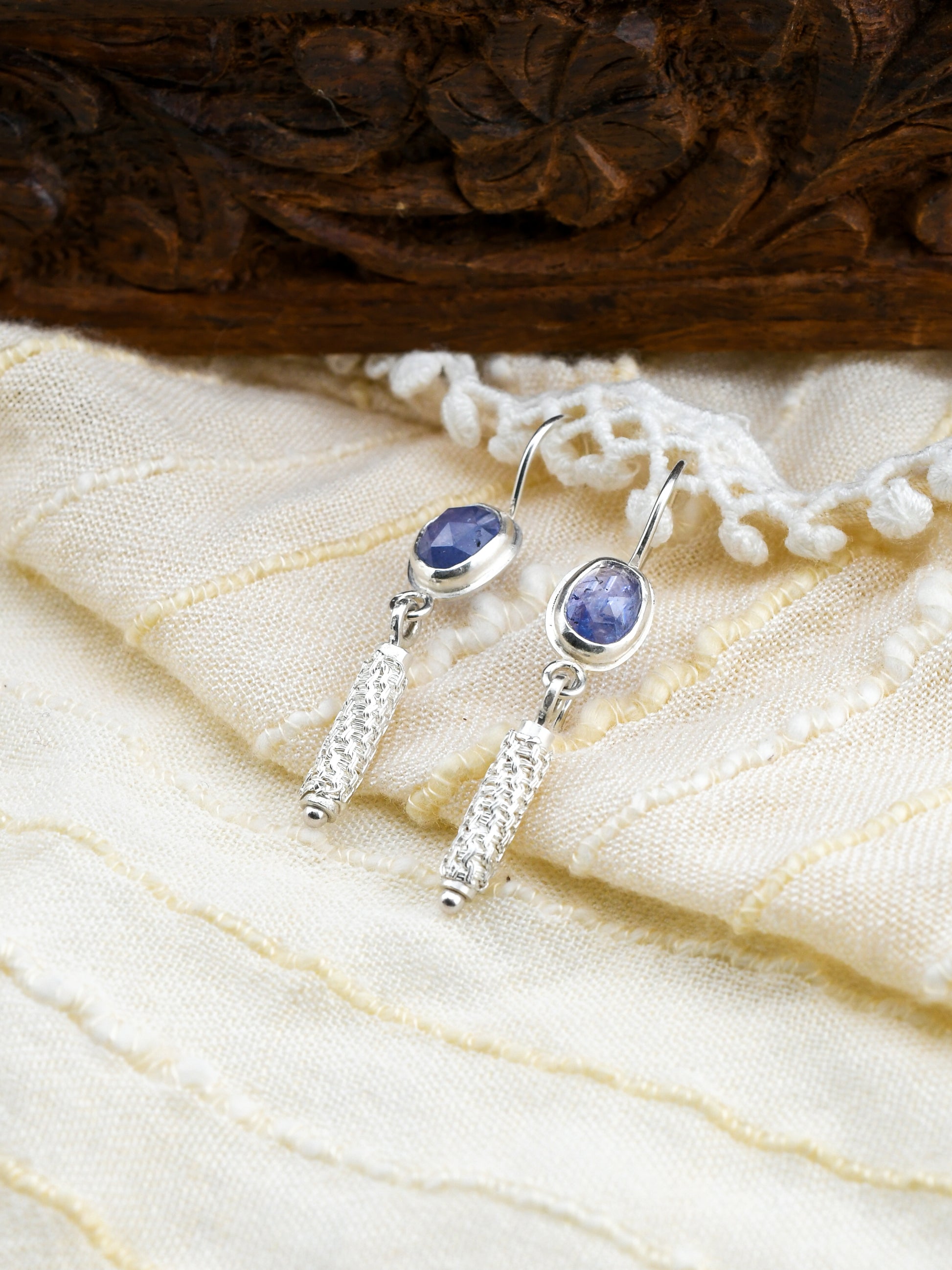 Silver earrings with blue gemstones on a textured fabric background