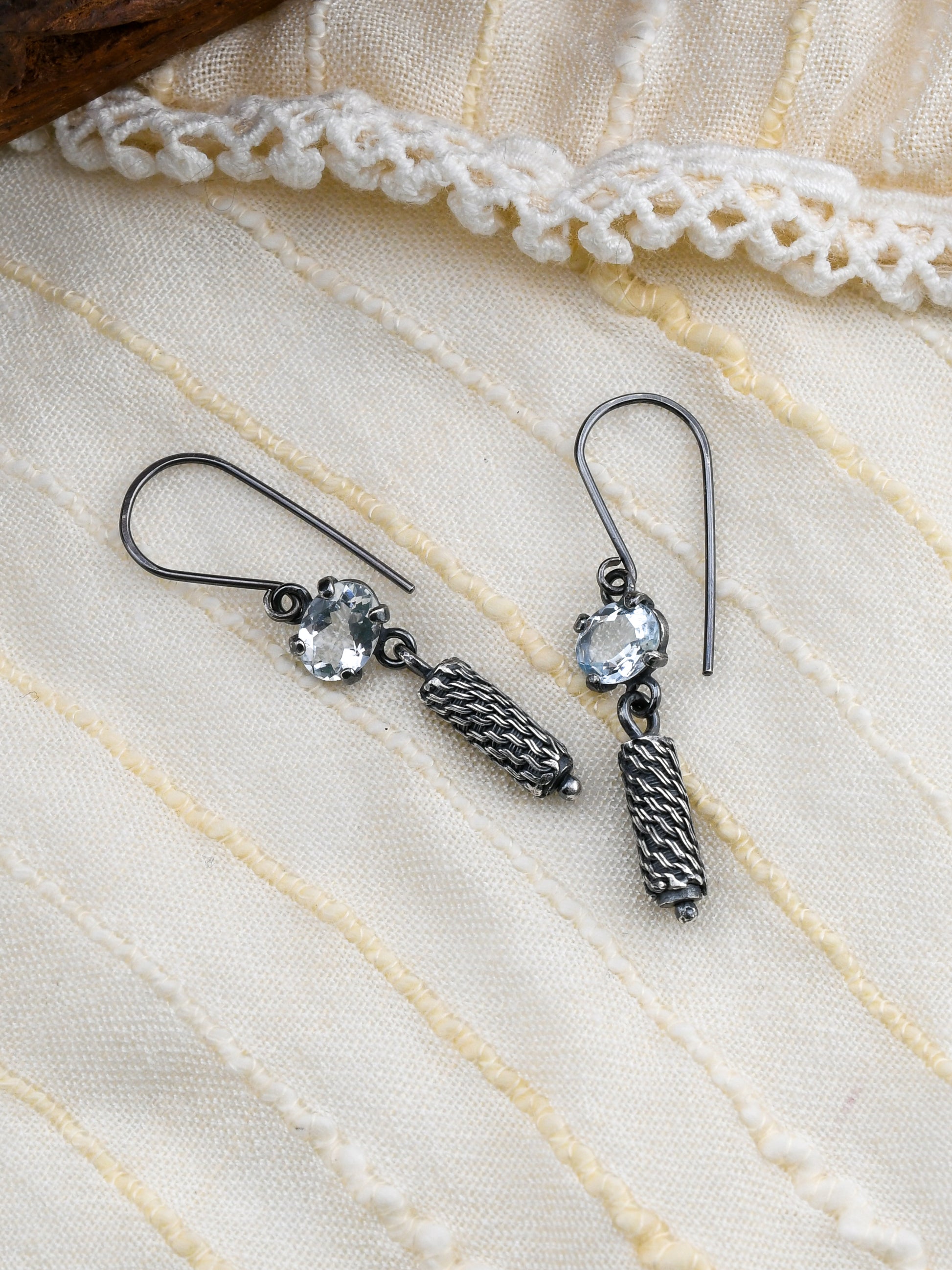 Silver earrings with pale blue gemstones on a textured white fabric background