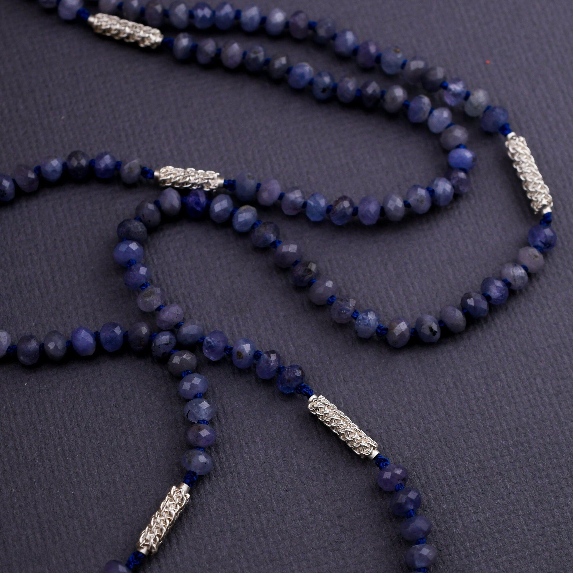 Blue beaded necklace with silver accents on a dark surface