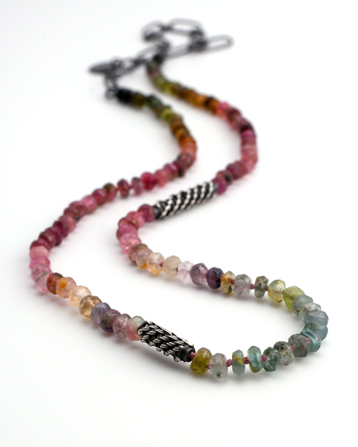 Multicolored natural tourmaline beaded necklace with woven silver bead accents and black silver chain extender on a white background