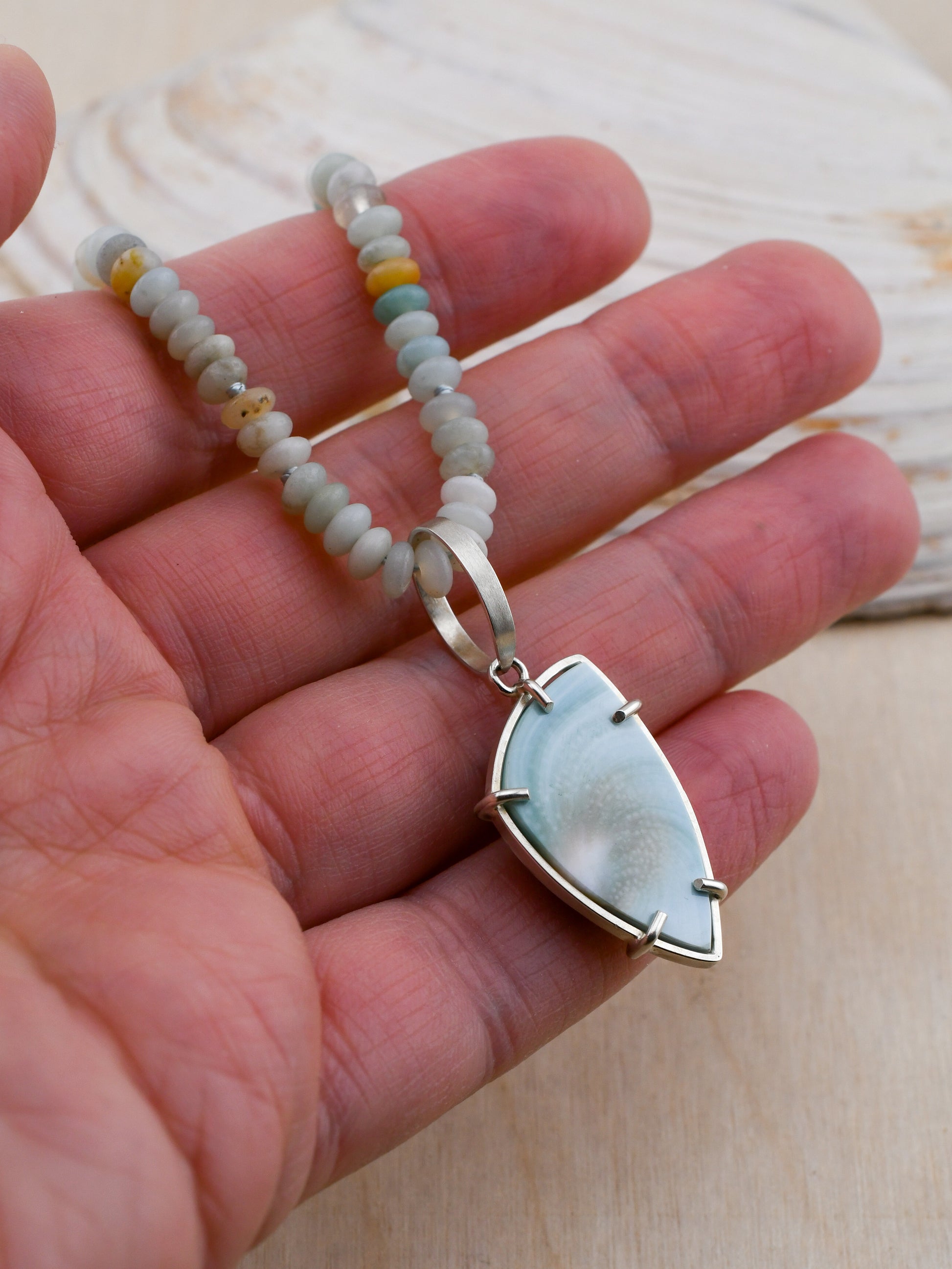 Hand holding a necklace with a silver pendant and beaded chain.