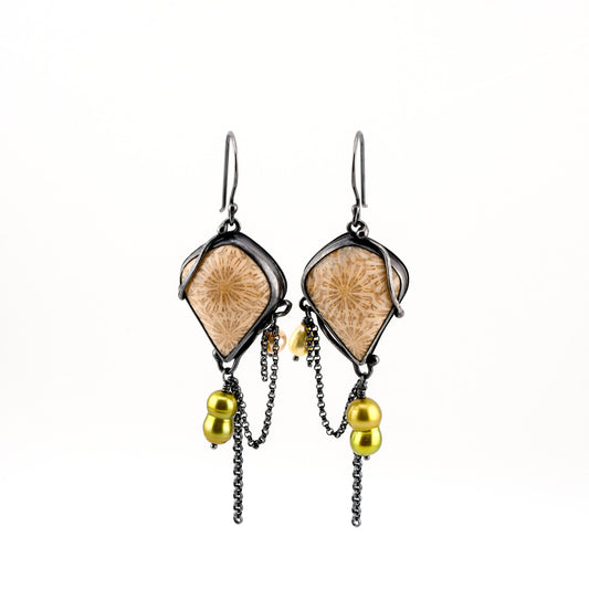 A pair of creamy fossilized coral earrings with gray flower patterns set in blackened silver with green and white baroque pearls drops on a white background