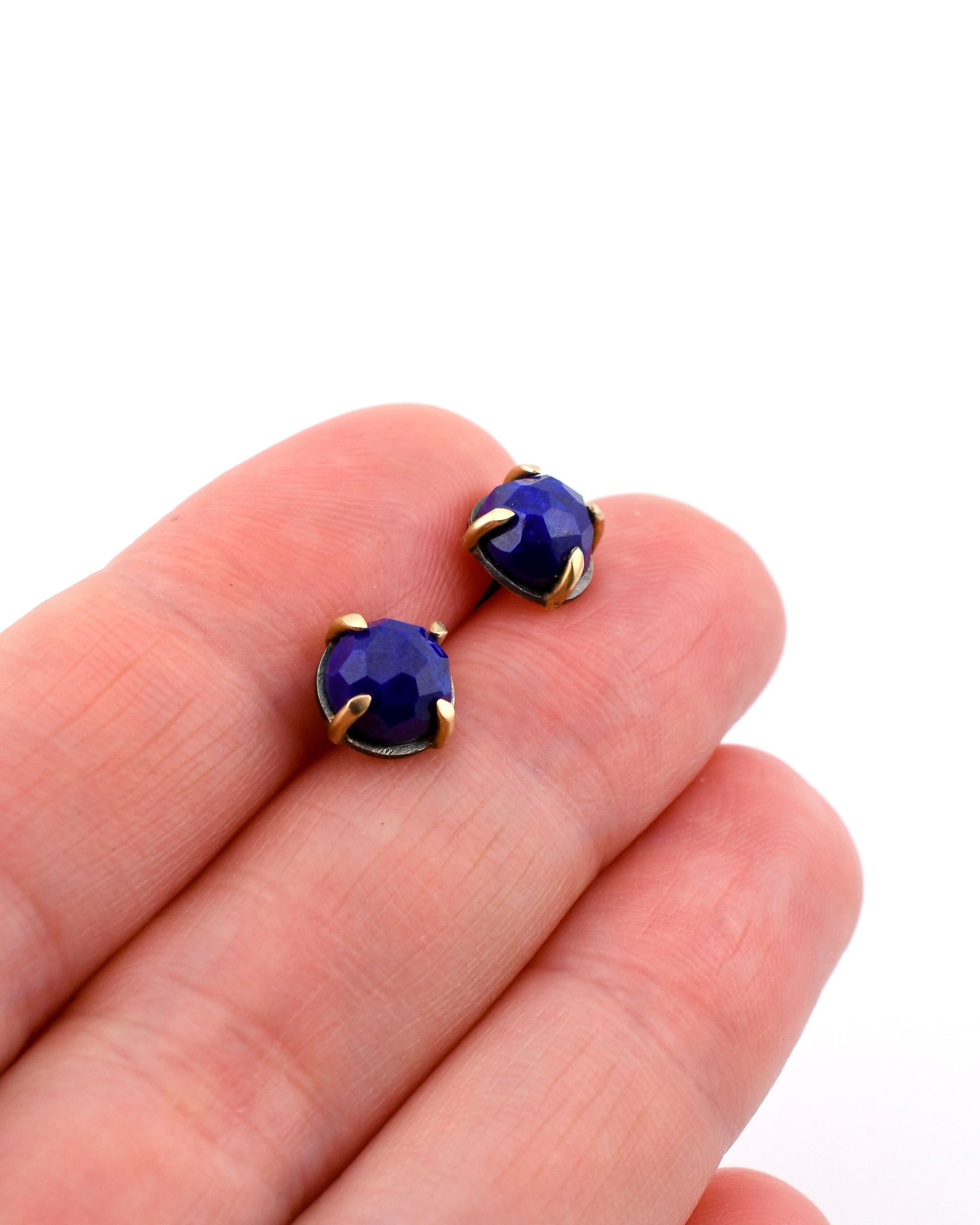 round lapis lazuli stud earrings in black silver and 14k gold held between fingers over a white background