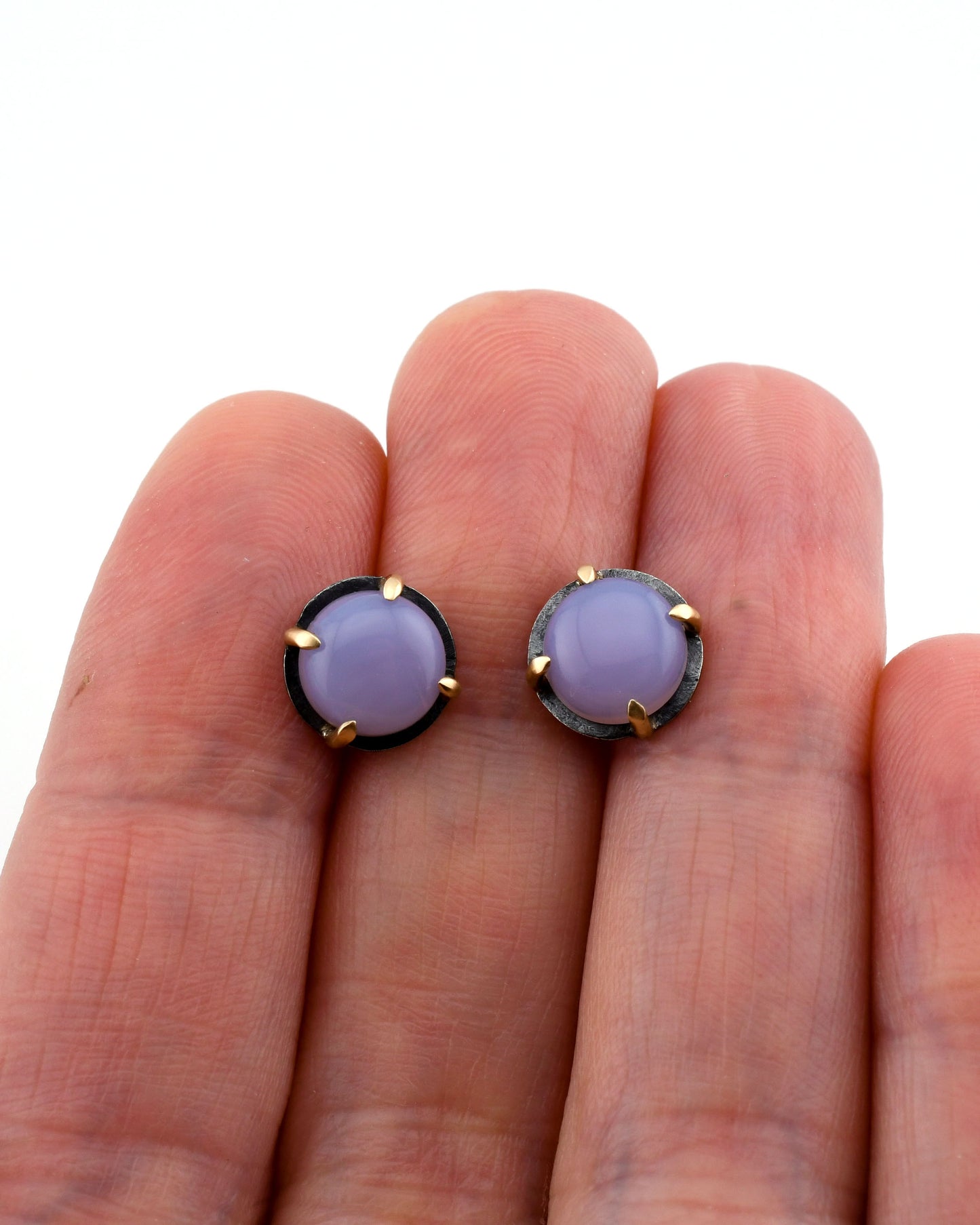 blackened silver and 14kg stud earrings with purple chalcedony held between fingers over a white background