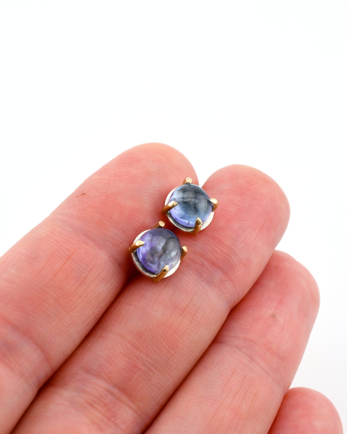 silver and gold round stud earrings with tanzanite held between earrings over a white background