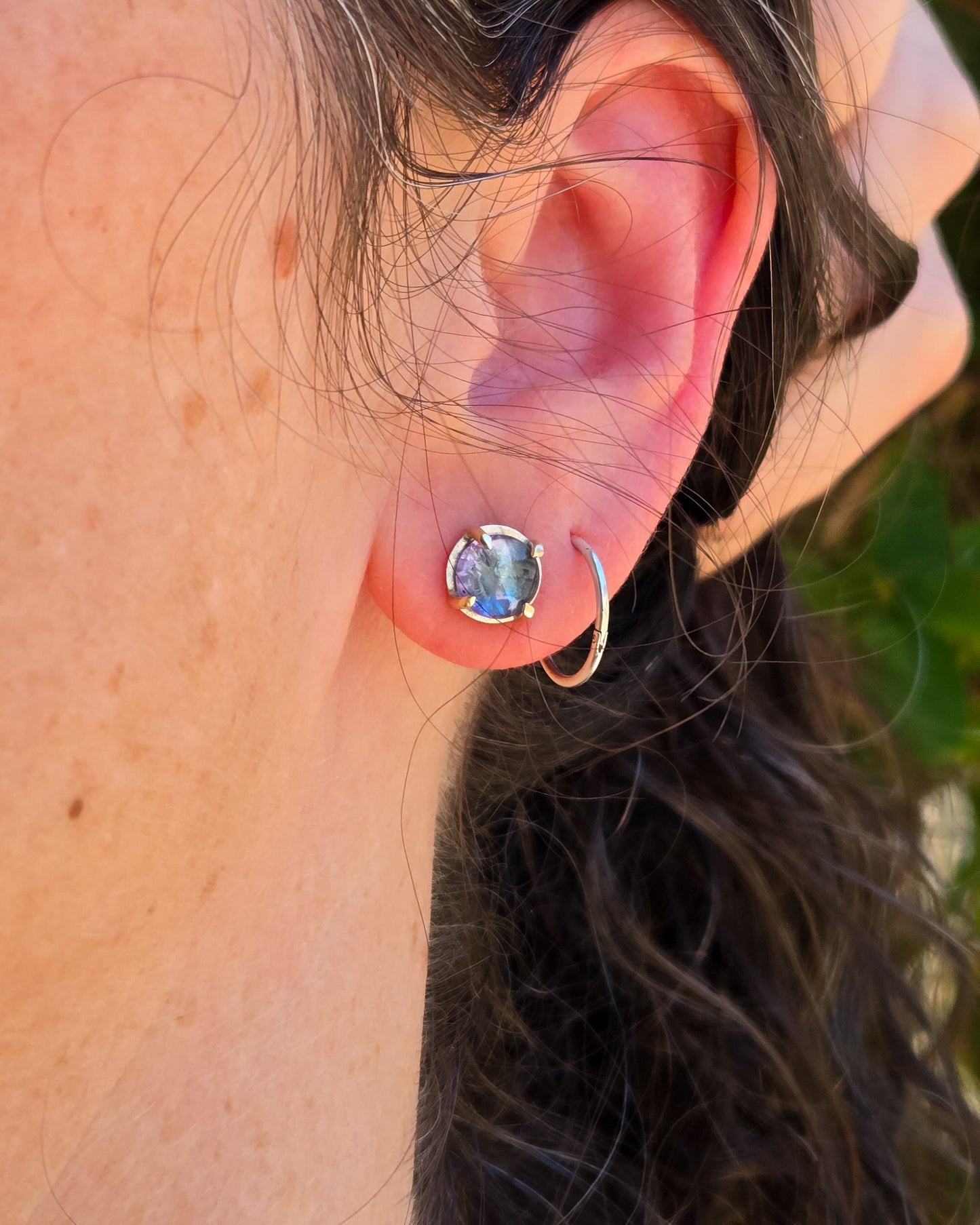 round silver and 14k gold studs with tanzanite shown worn on an ear in natural light
