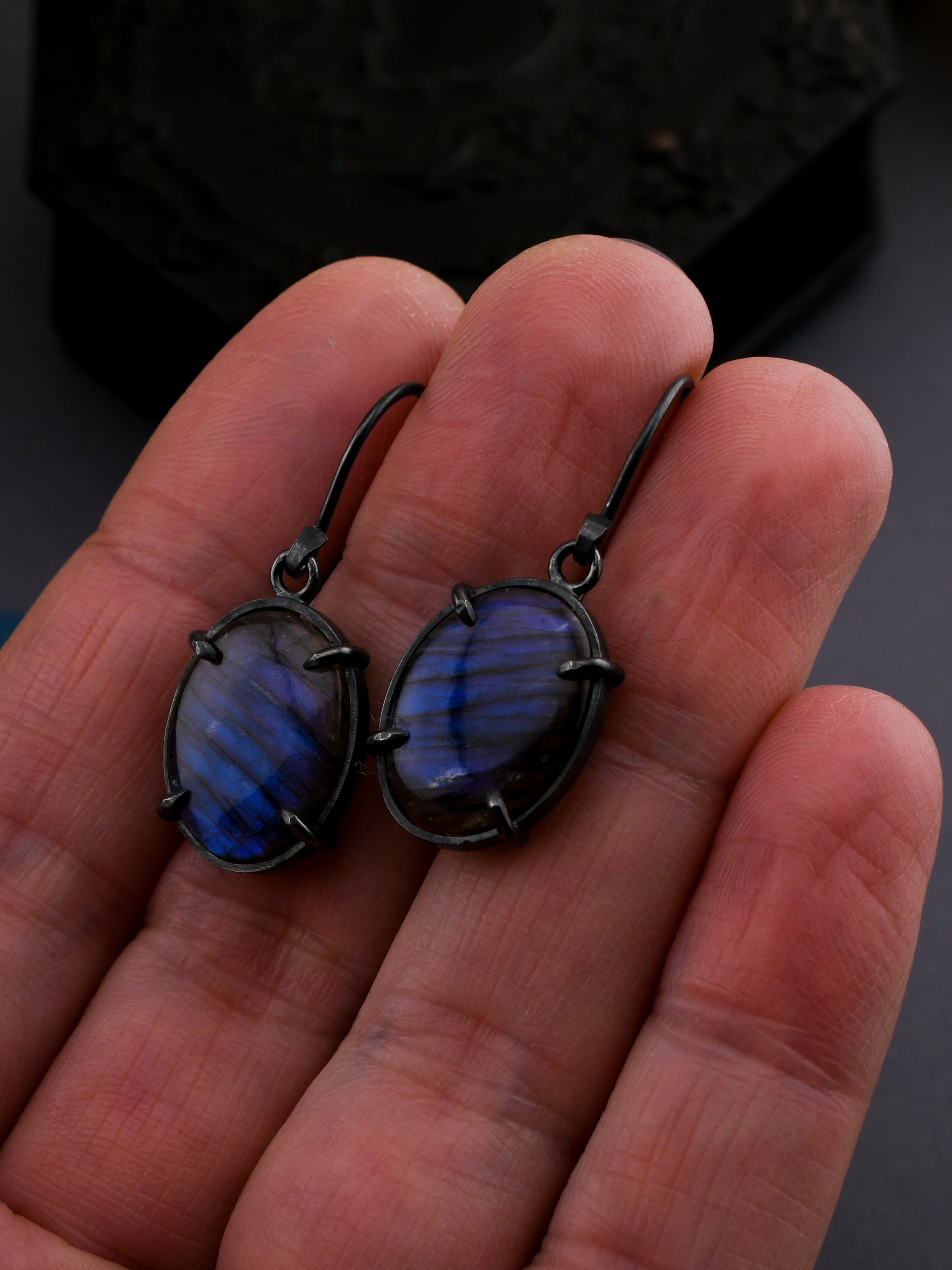 Blue stone earrings held in a hand against a dark background
