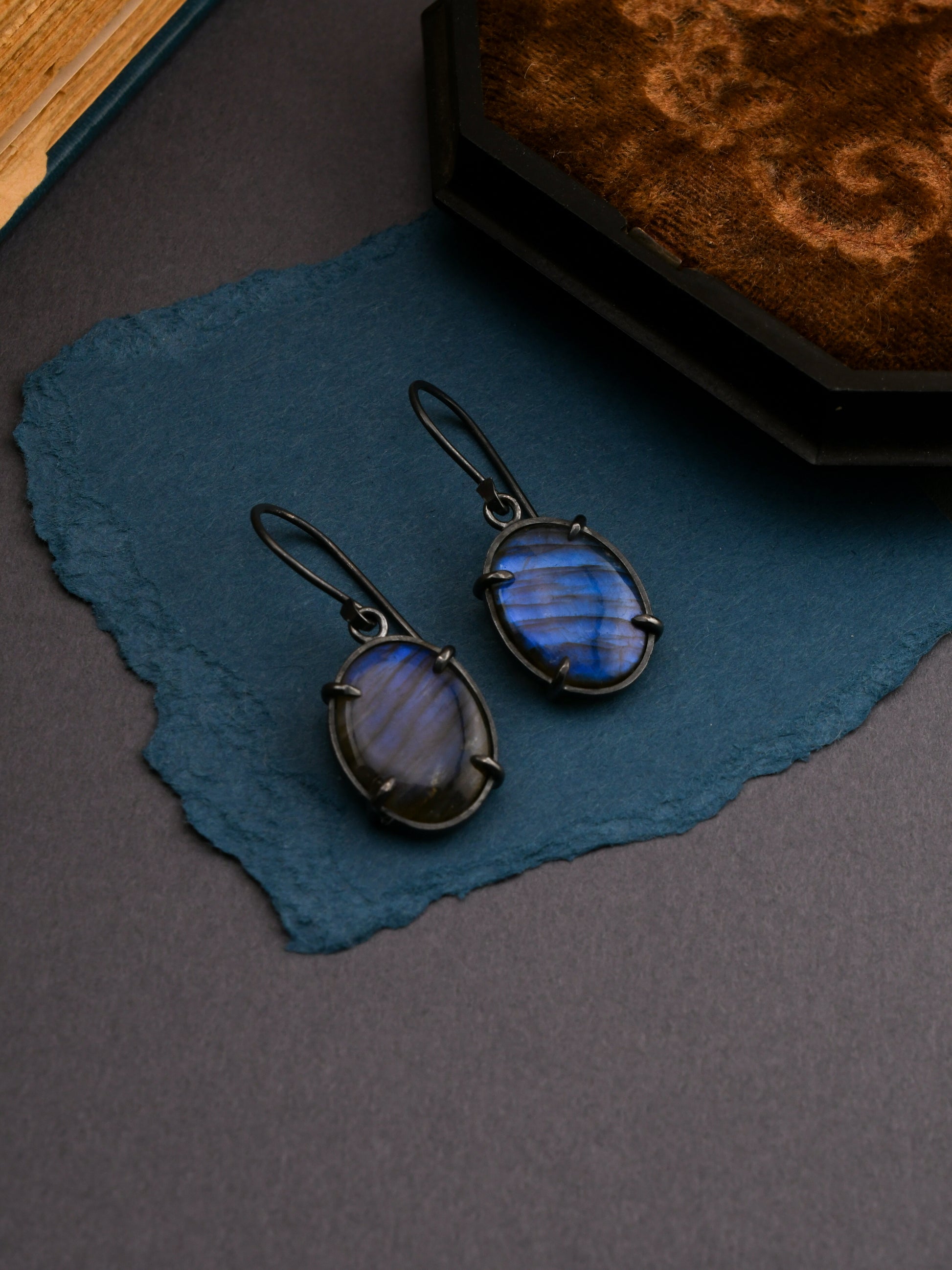 Blue gemstone earrings on a textured blue surface with a dark background