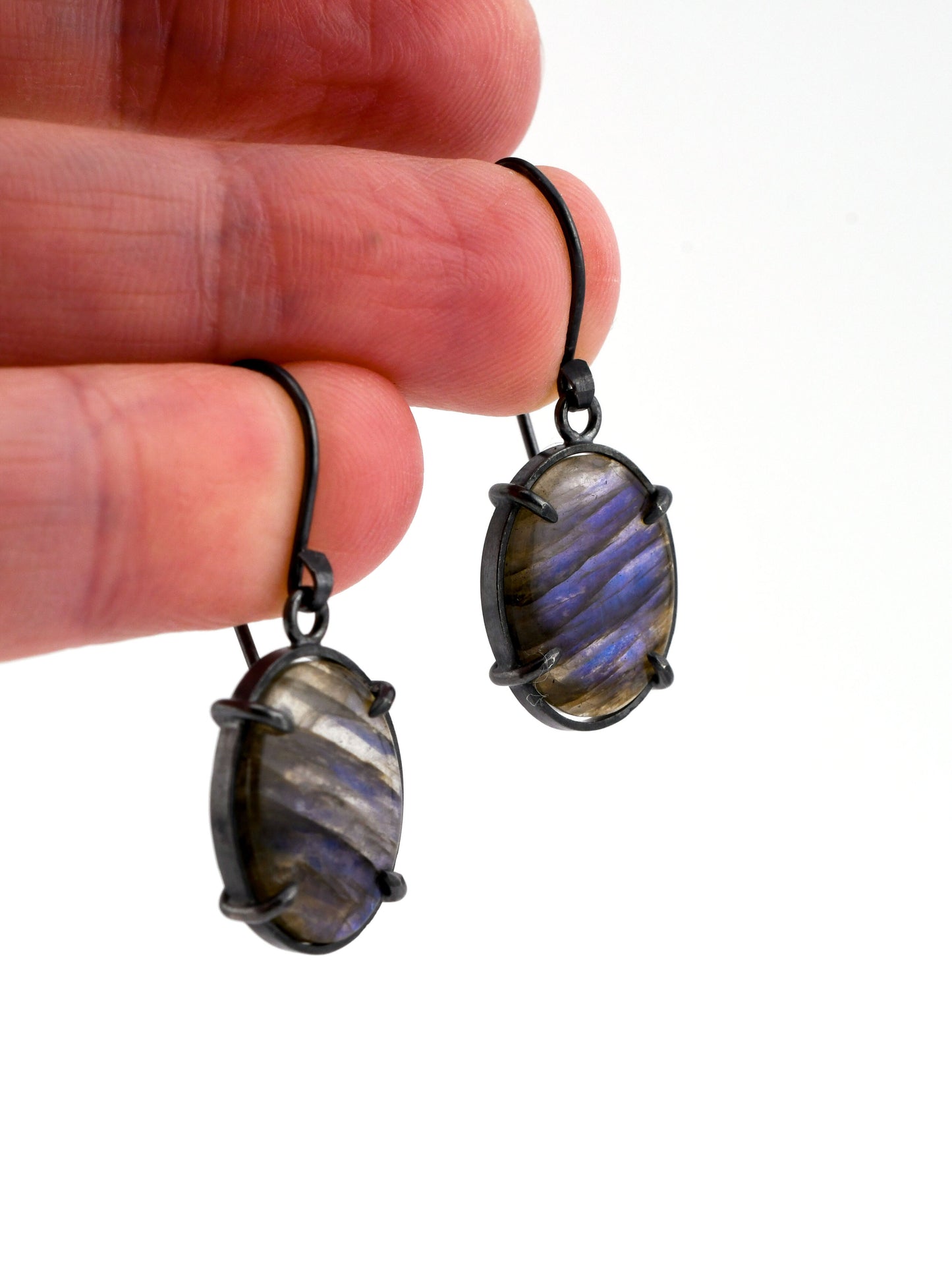 Pair of labradorite earrings held between fingers on a white background