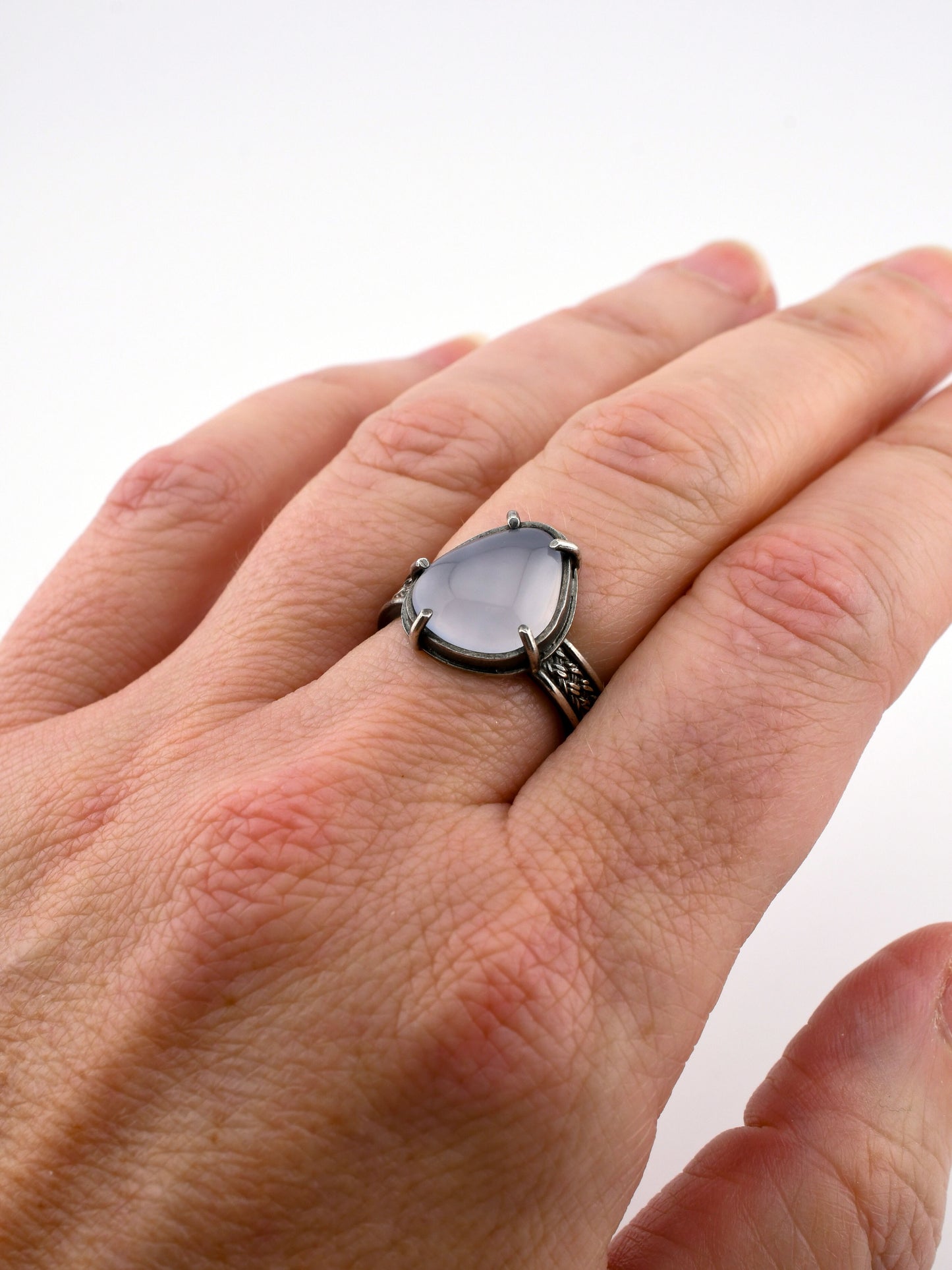 Hand wearing a silver ring with a lavender stone on a white background