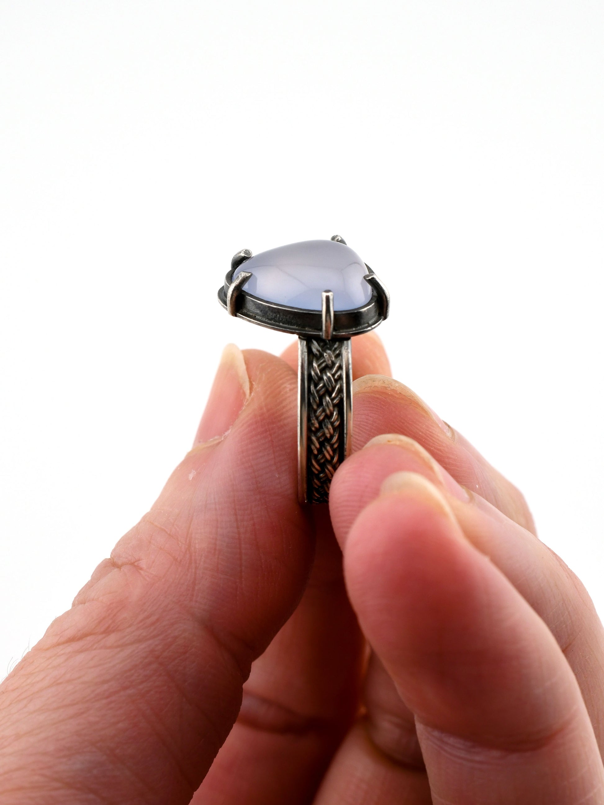 Hand holding a ring with a pale lavender gemstone on a white background