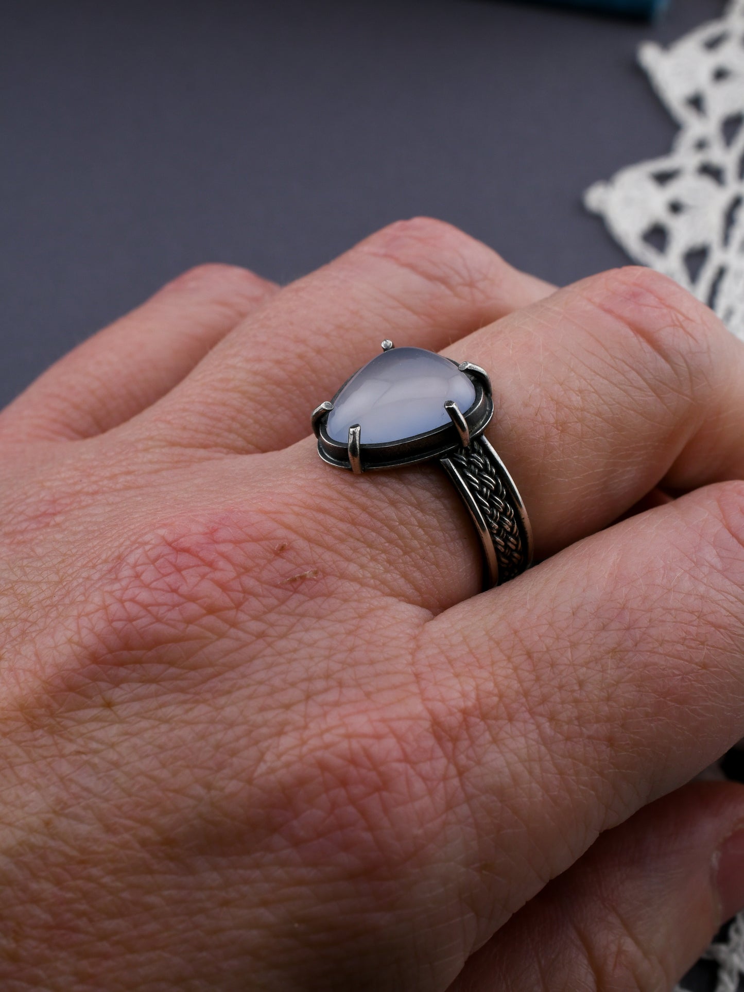 Hand wearing a ring with a lavender gemstone on a dark background