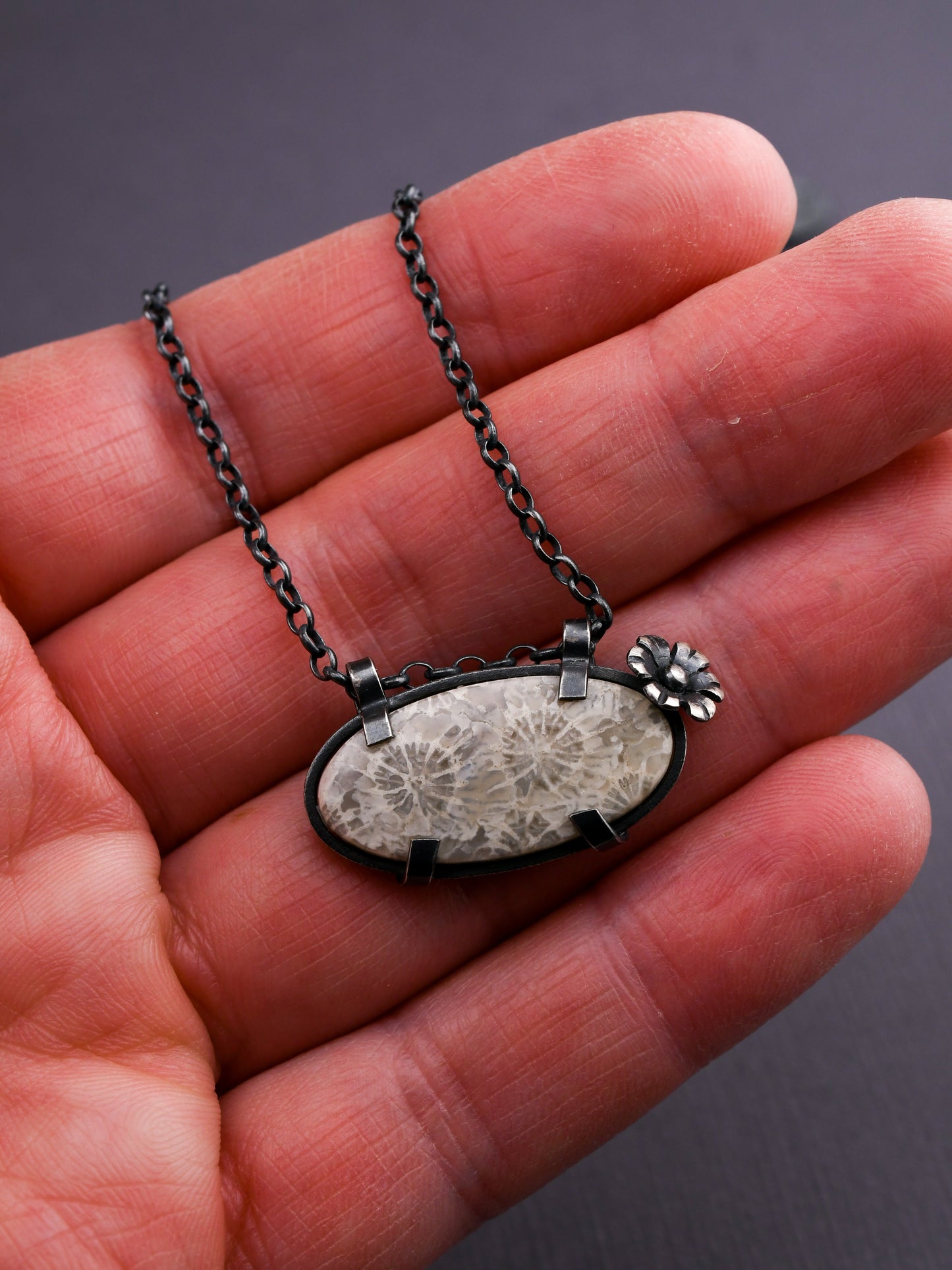 Necklace with a pendant held in a hand against a dark background