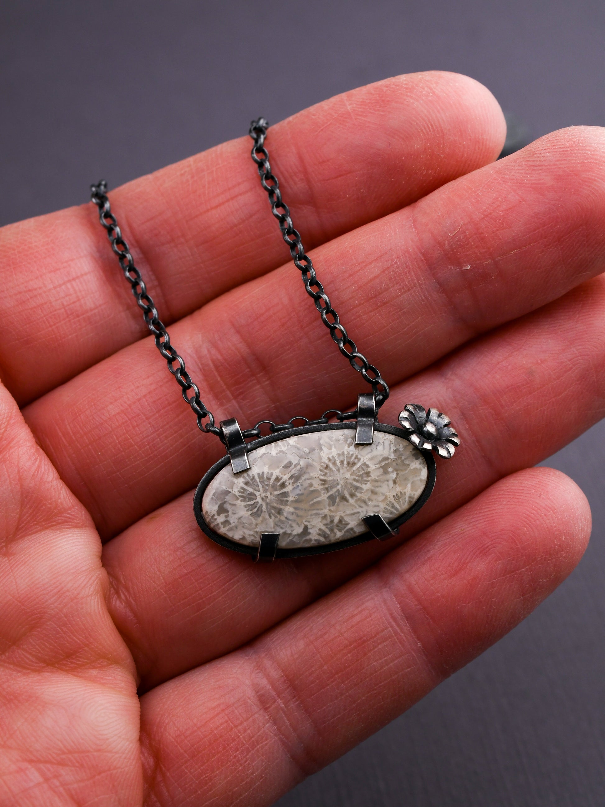 Necklace with a pendant held in a hand against a dark background