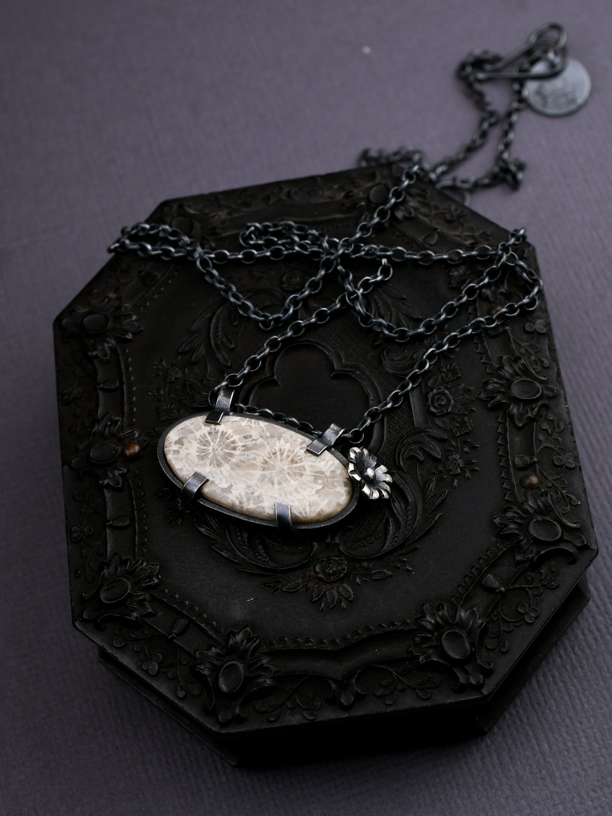 Necklace with a pendant on a dark, ornate stand against a dark background