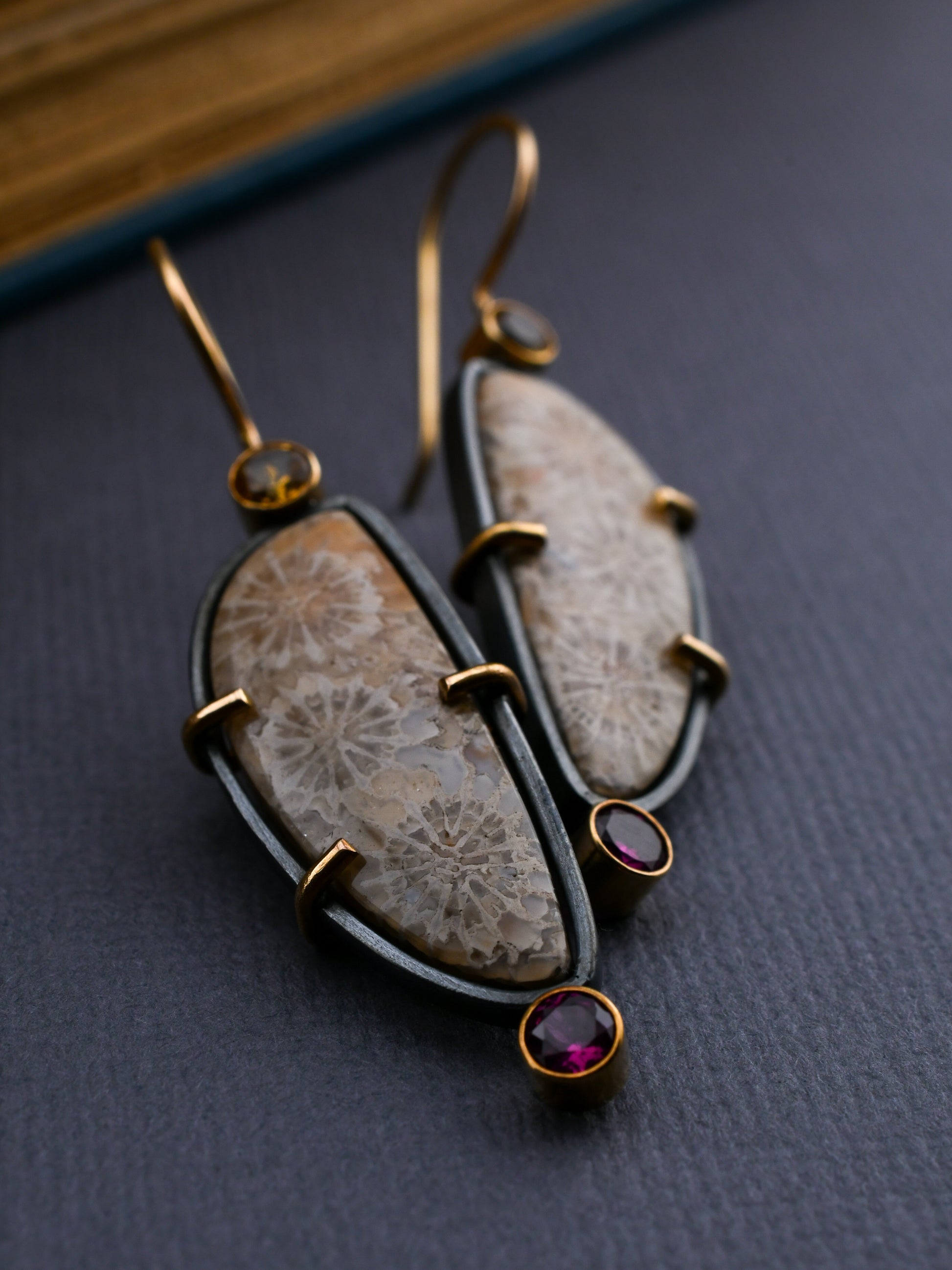 Pair of earrings with fossilized coral and gemstones on a dark surface