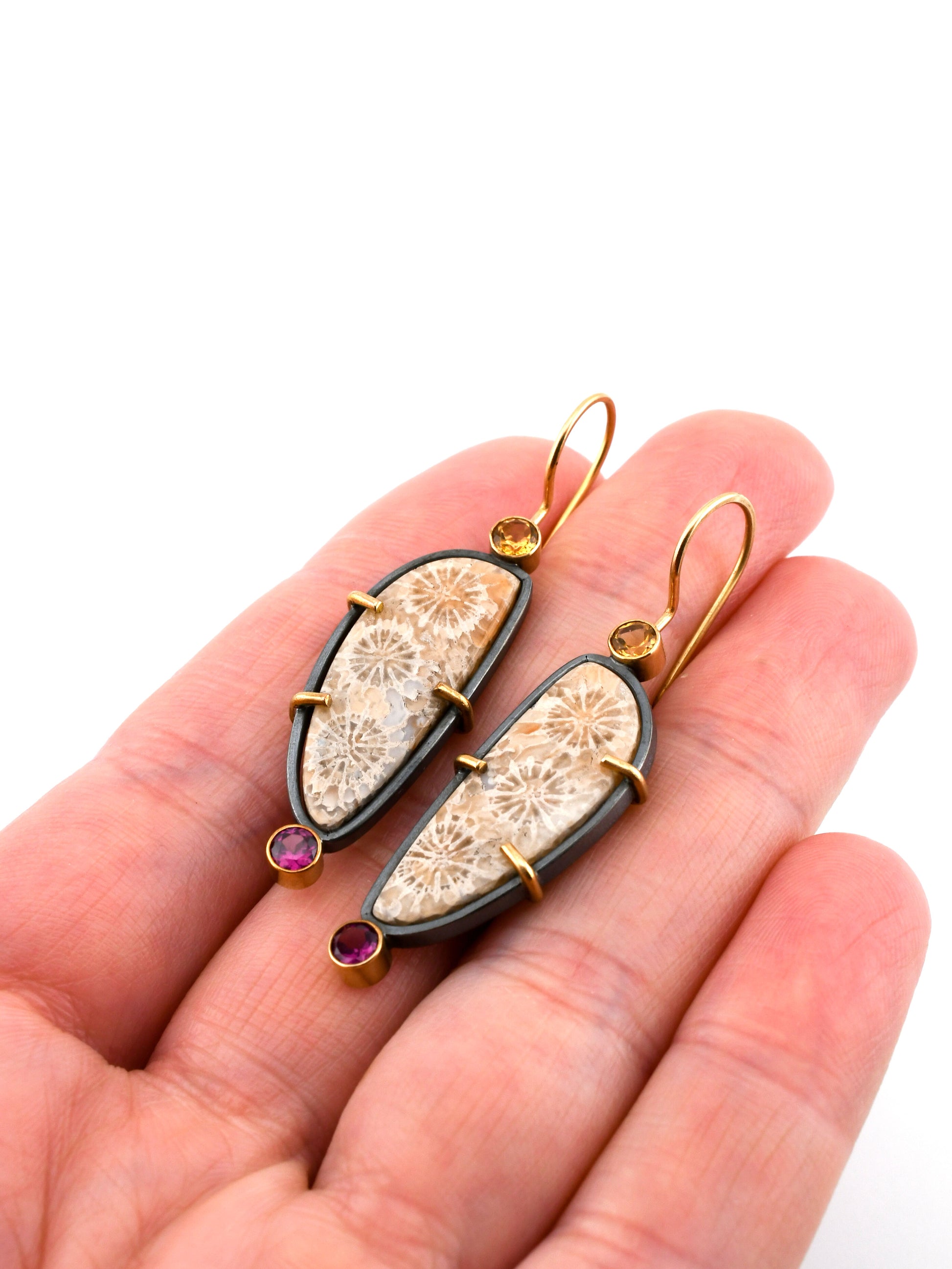Pair of decorative earrings held in a hand with a white background