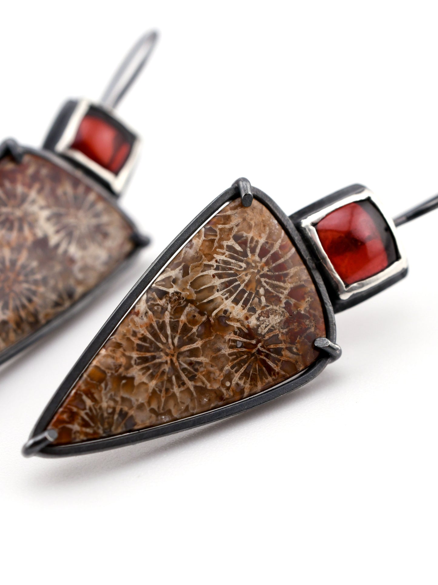 Earrings set with triangular brown stone and red gemstone on a white background